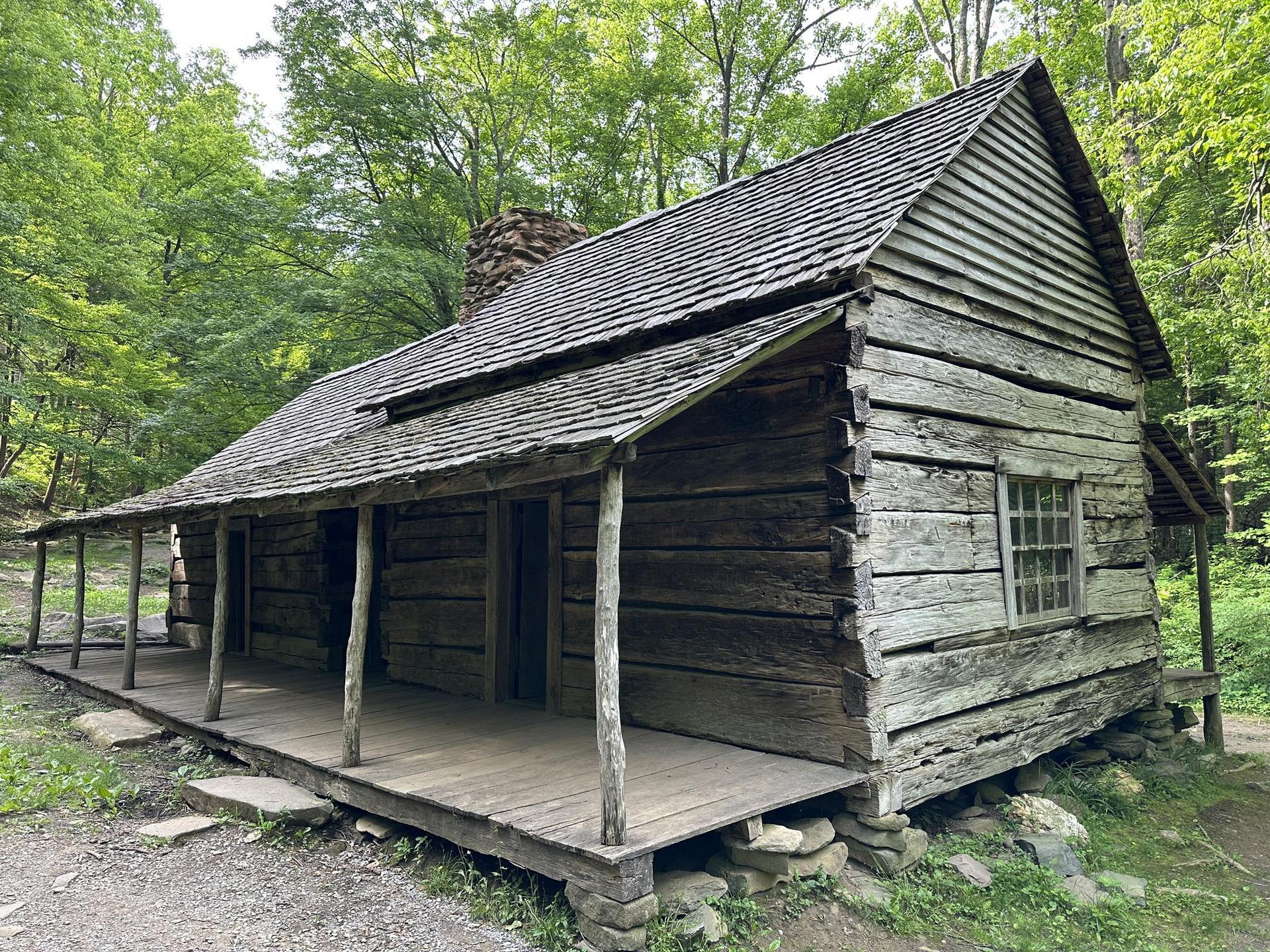 Rustic wooden log cabin with a porch, nestled among green trees.