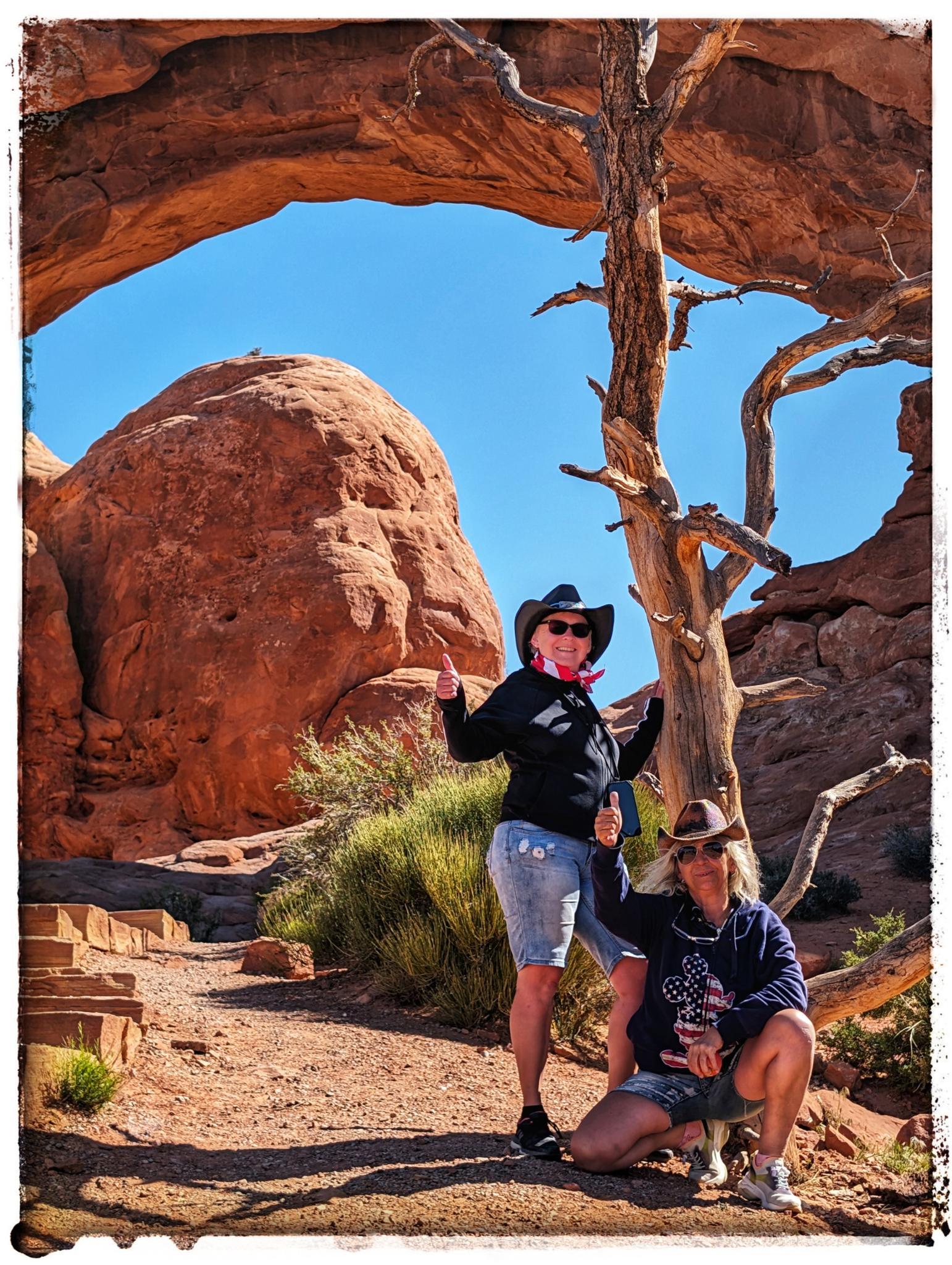 Two women posing with thumbs up under a natural rock arch.