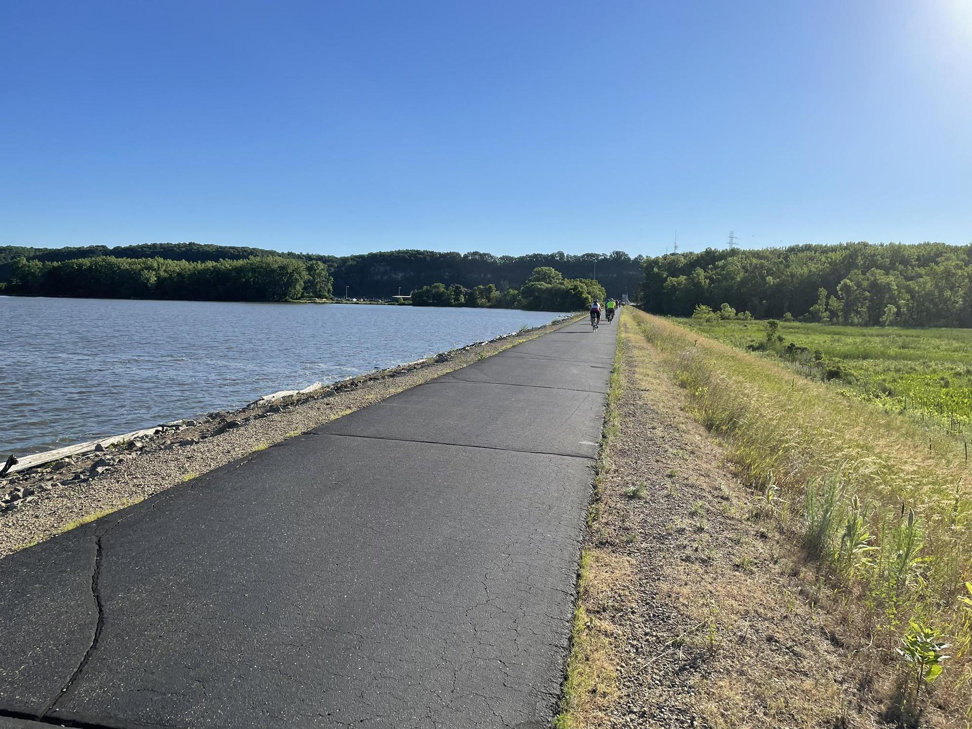 Paved path alongside a lake with distant people on a sunny day.