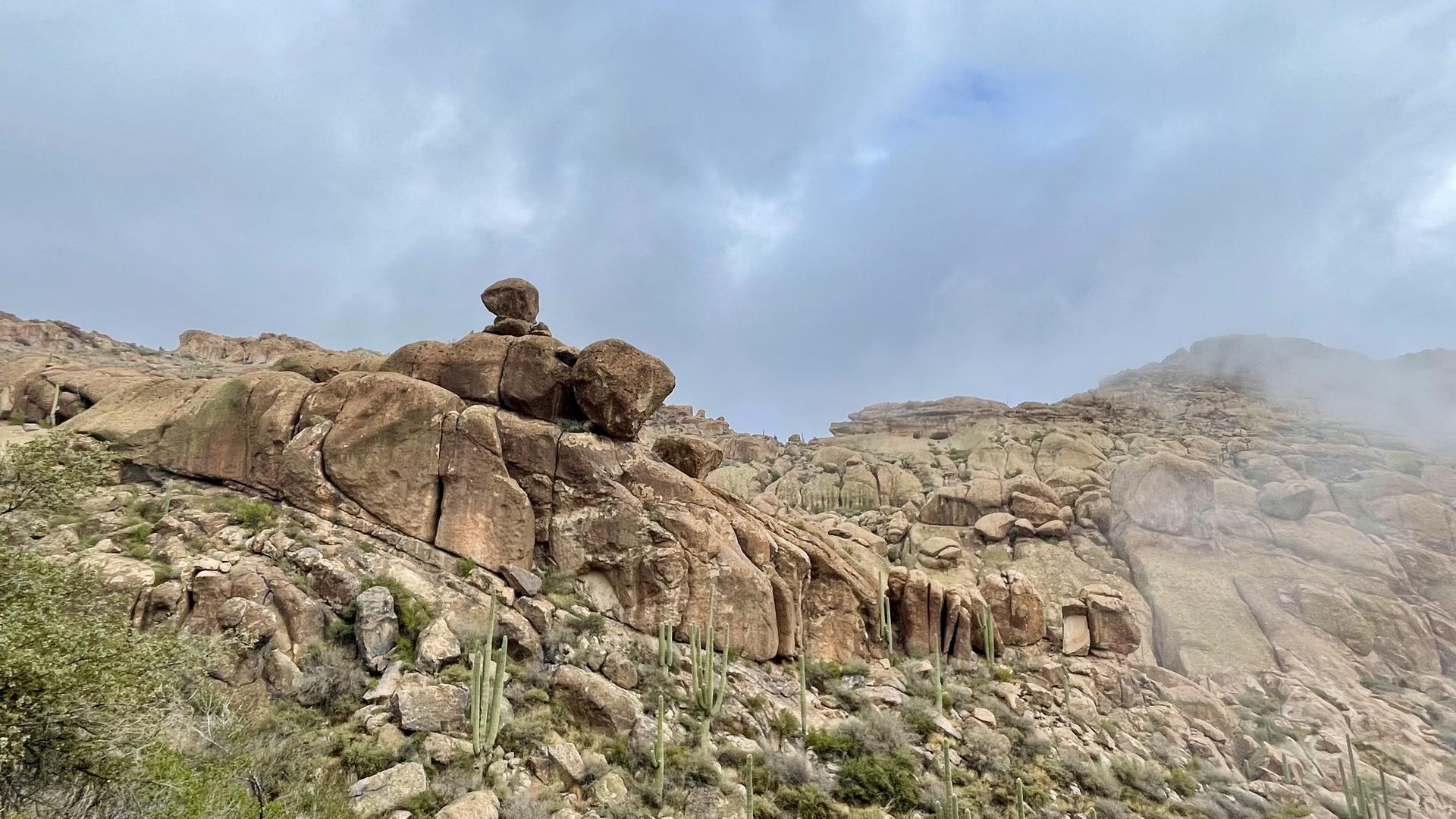 Rocky desert mountains with a balanced rock formation under a cloudy sky.
