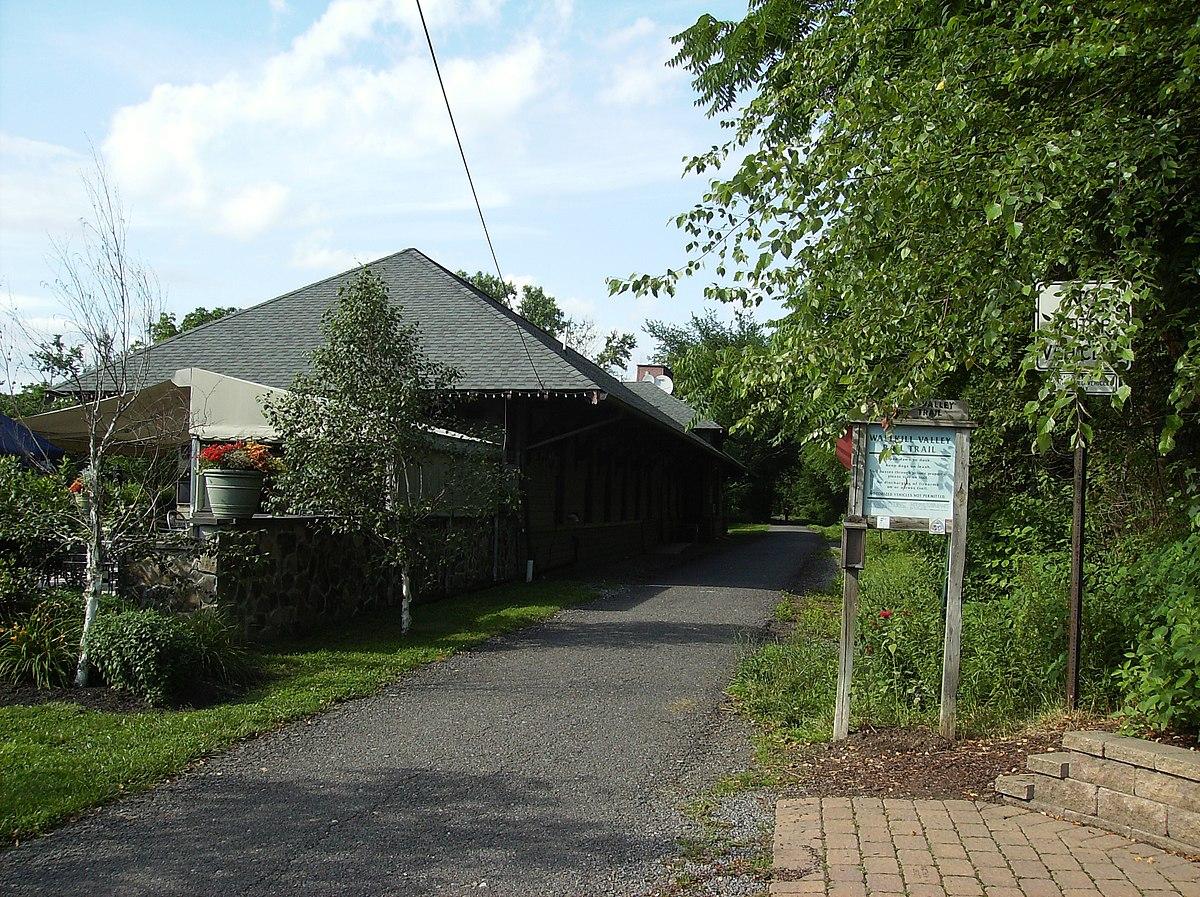Daylight view of a building with a dark roof, a path, and lush greenery.