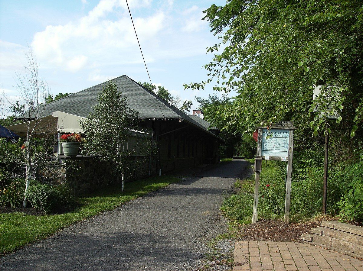 Daylight view of a building with a dark roof, a path, and lush greenery. - Wallkill Valley Rail Trail