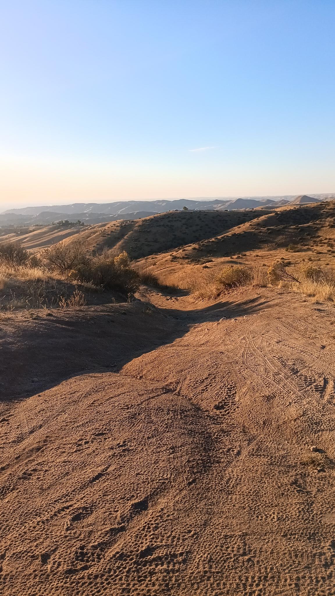 Sandy, rocky terrain with tire tracks, bathed in warm golden hour light.