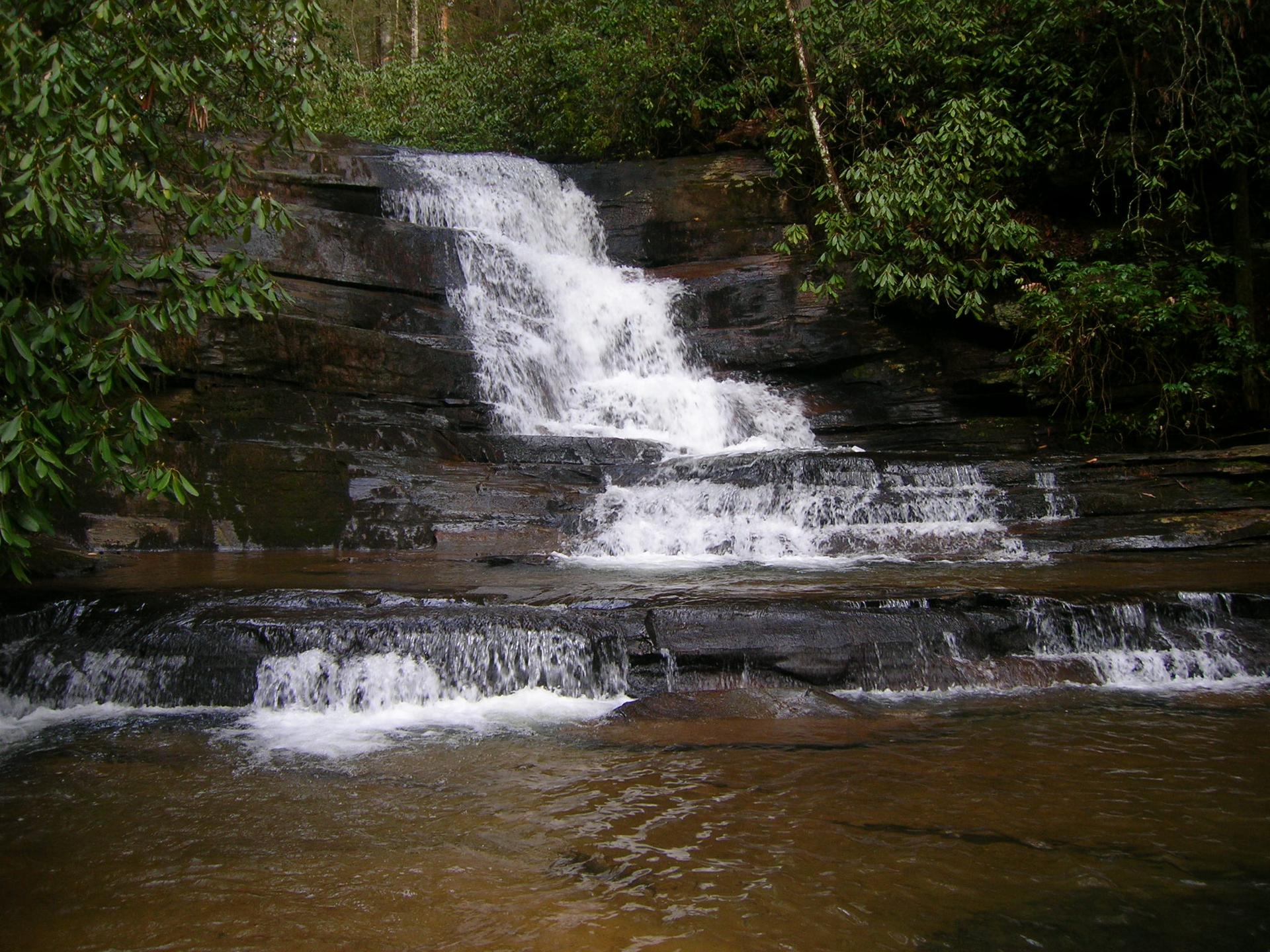 A multi-tiered waterfall cascades over dark rocks into a calm pool.