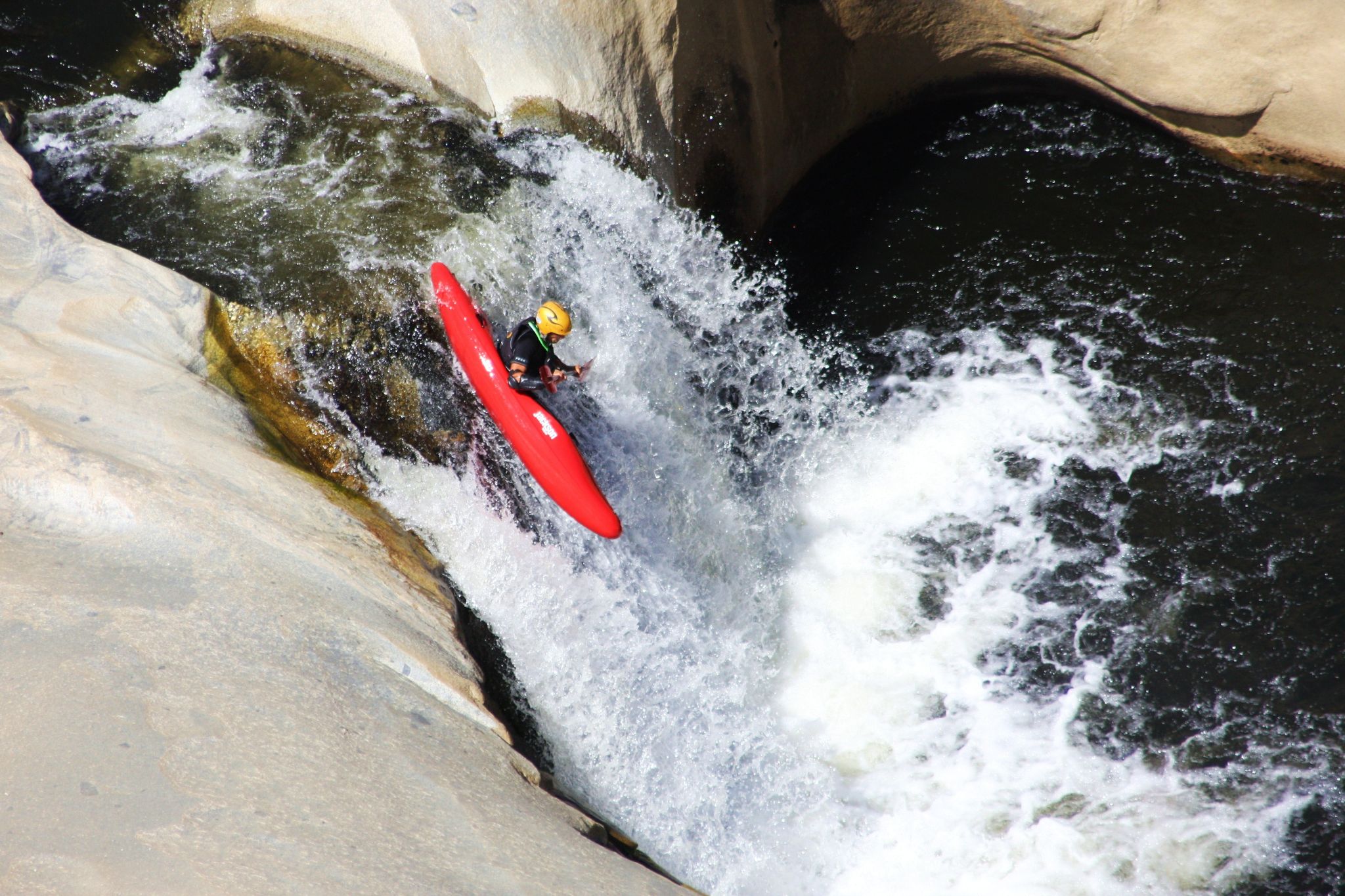 Kayaker in red boat plunges down a rocky waterfall in bright sunlight. - Seven Tea Cups Viewpoint via Dry Creek Meadow