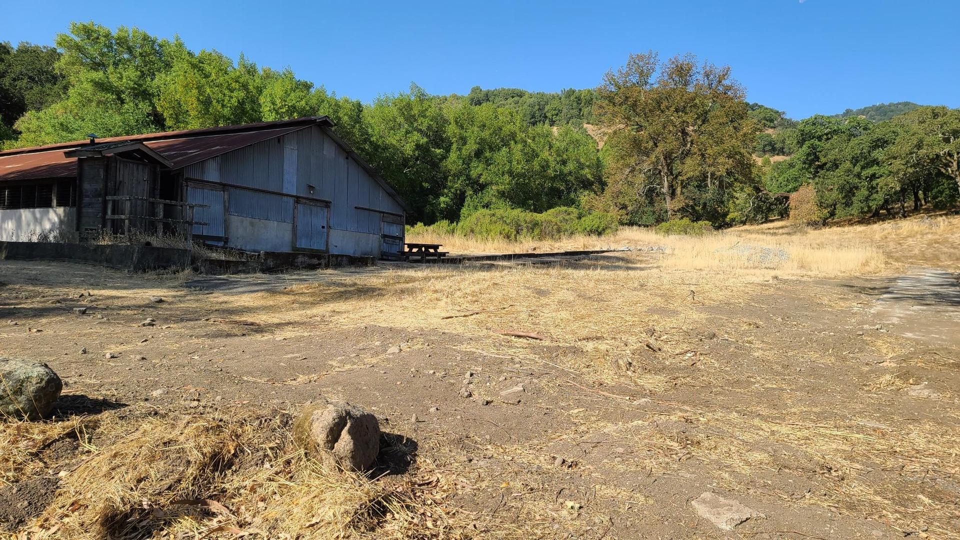 An old barn stands in a dry, dusty field under a clear sky.