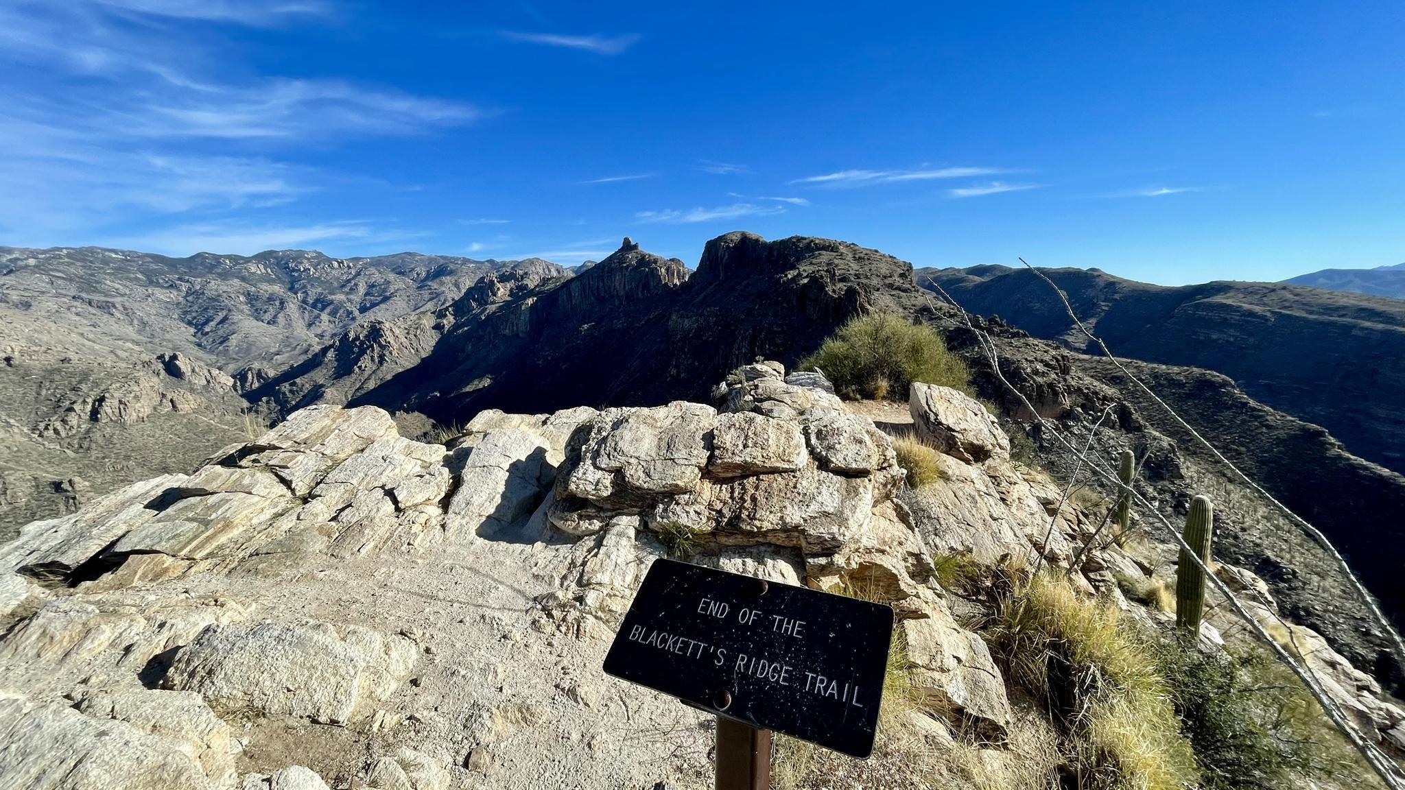 Sign on a rocky mountain peak overlooking a vast, rugged landscape.
