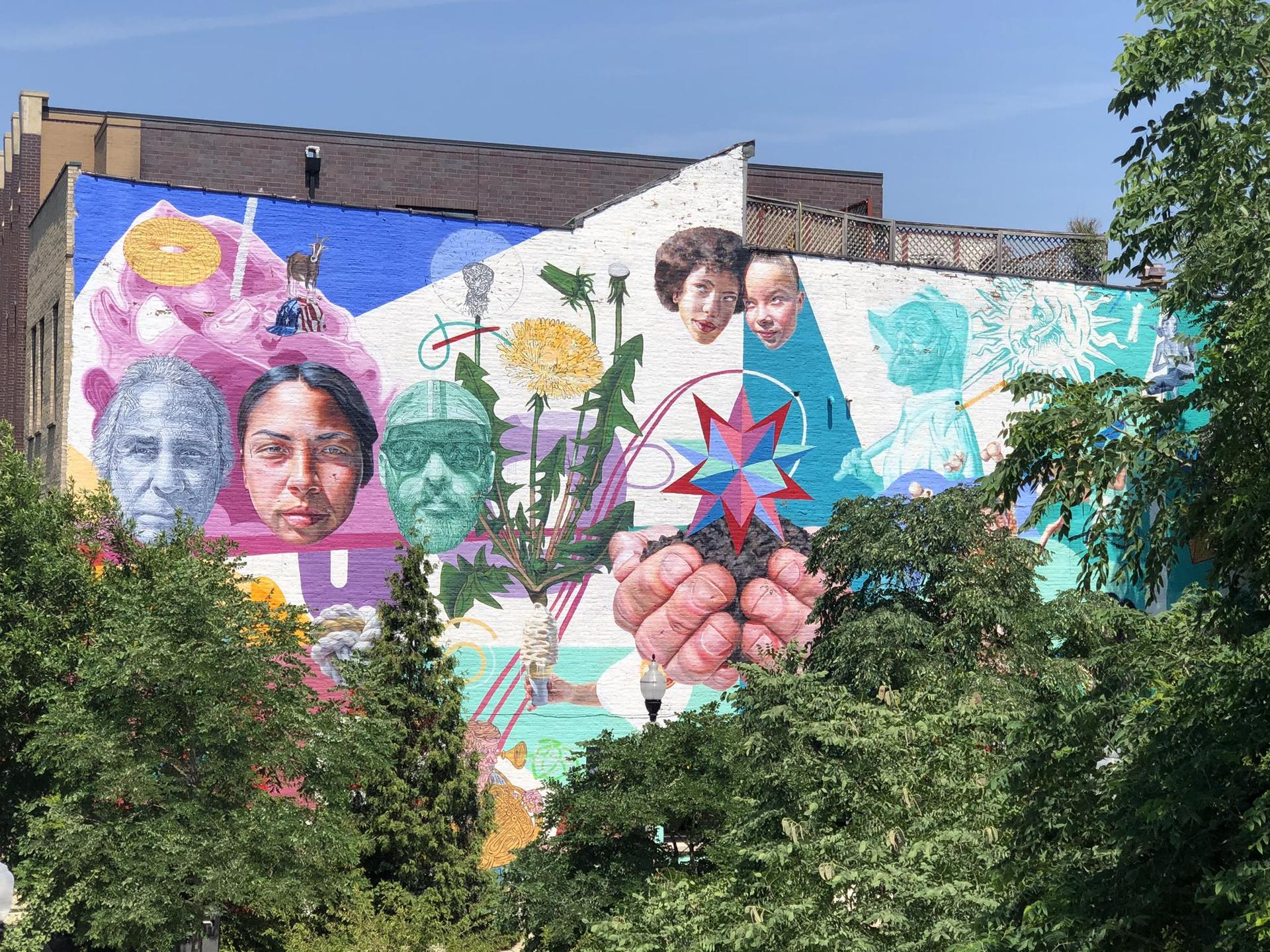 Large, colorful mural on a building wall, partially obscured by green trees.