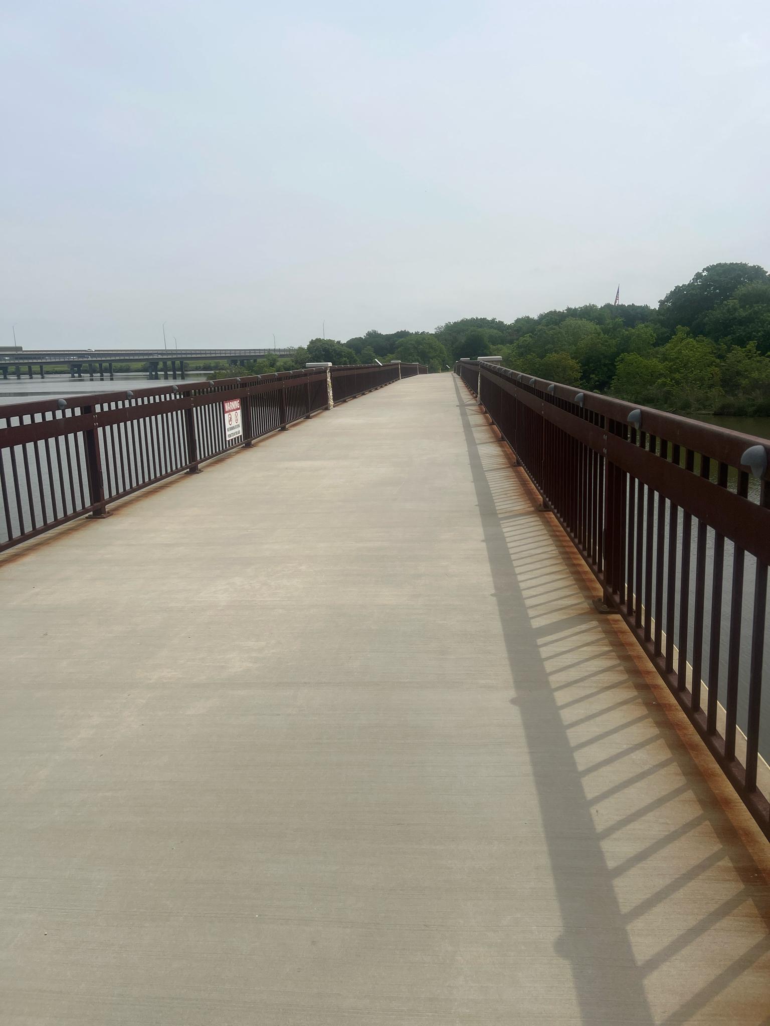 Wide concrete bridge with metal railings extending over water under a hazy sky.