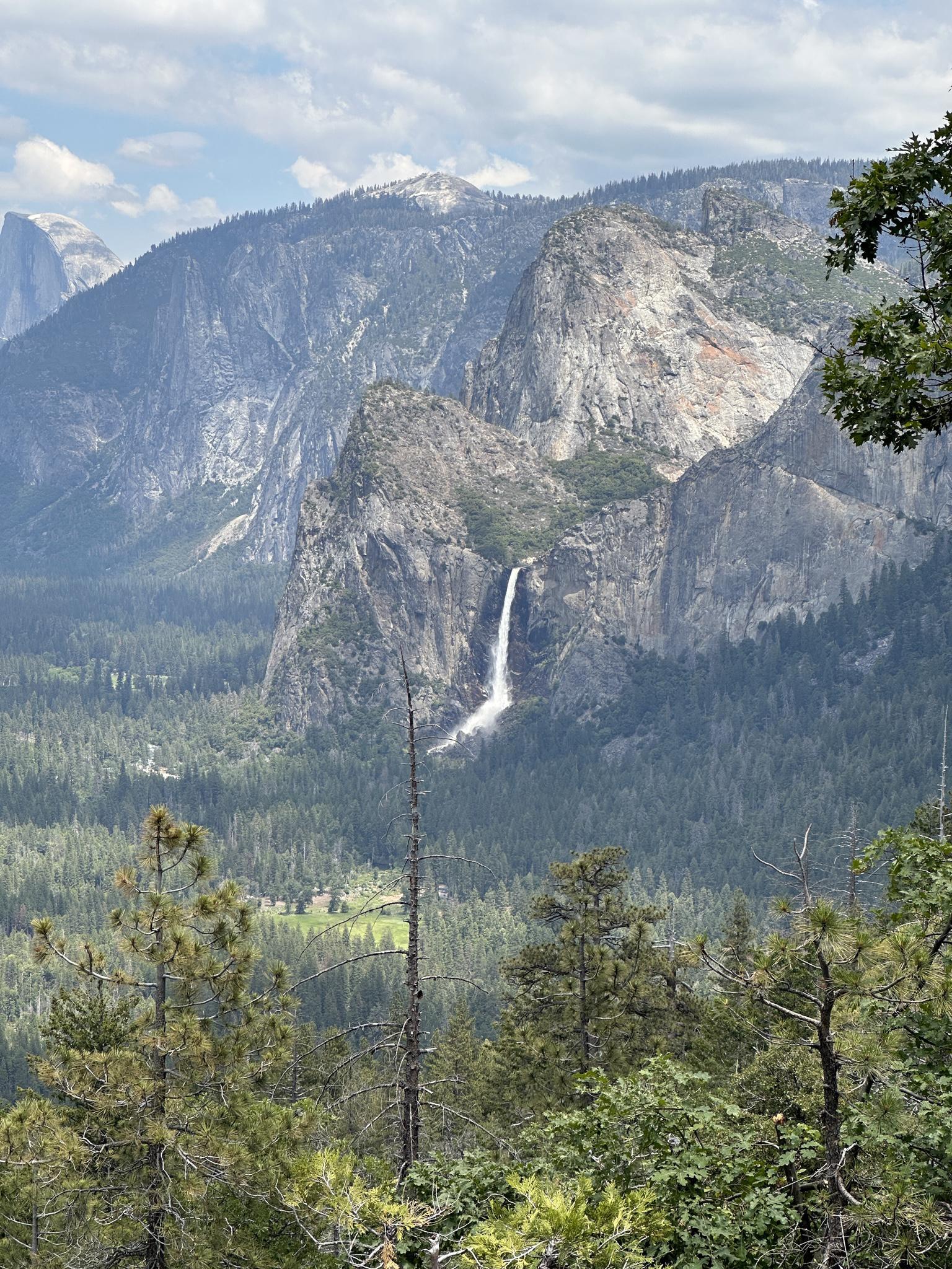 Distant waterfall cascading down a rocky mountain face, surrounded by trees.