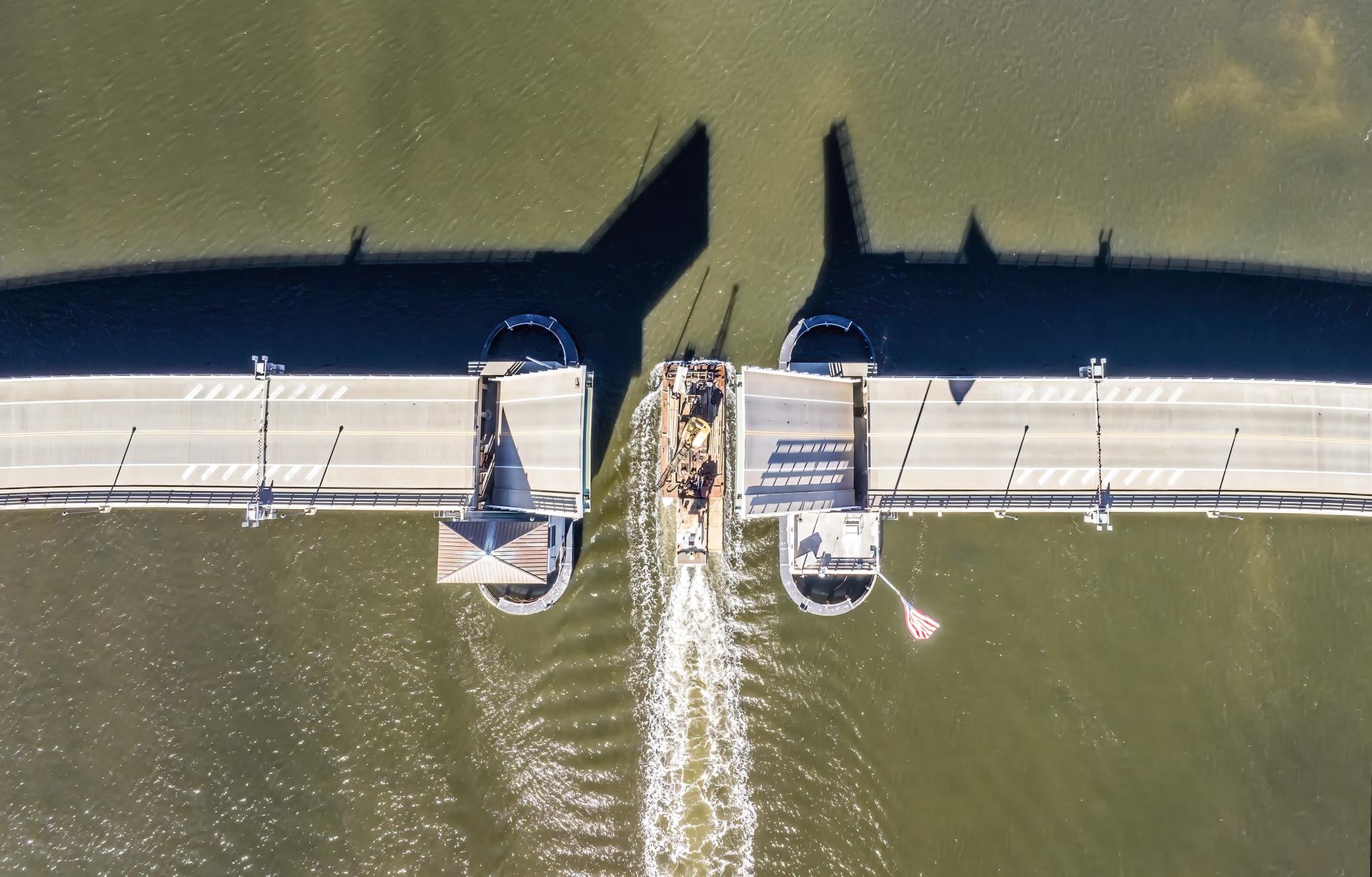 Aerial view of a boat passing through an open drawbridge on water.