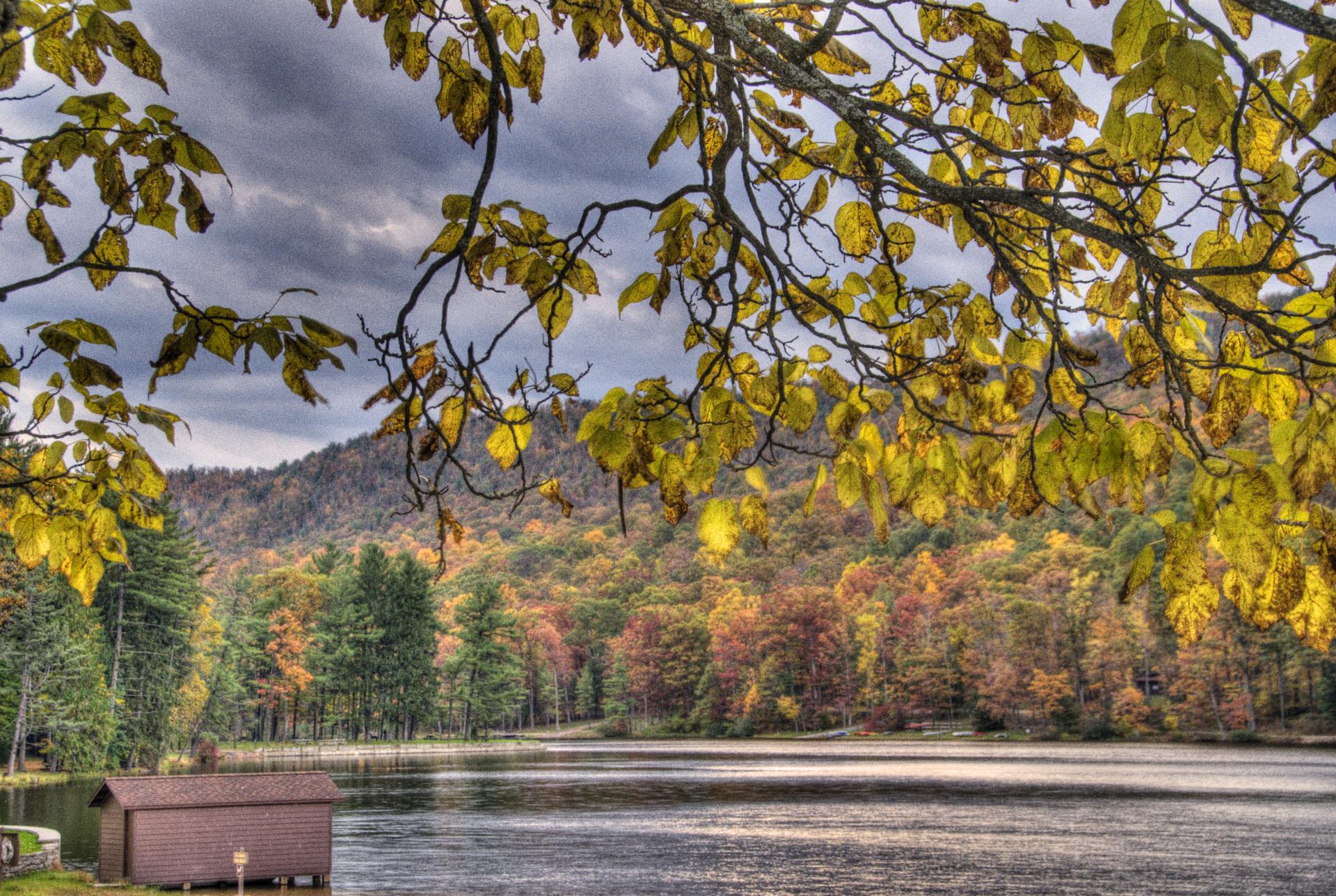 A boathouse on a lake surrounded by autumn trees under a cloudy sky.