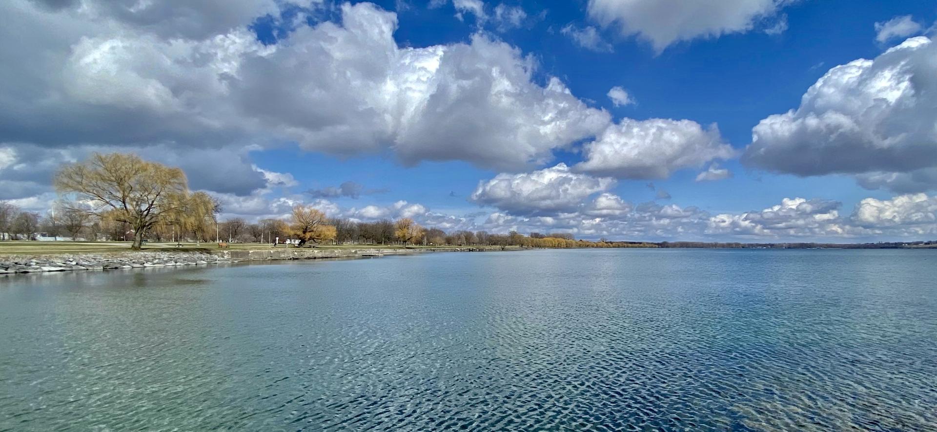 An expansive lake with a tree-lined shore under a dramatic cloudy sky.