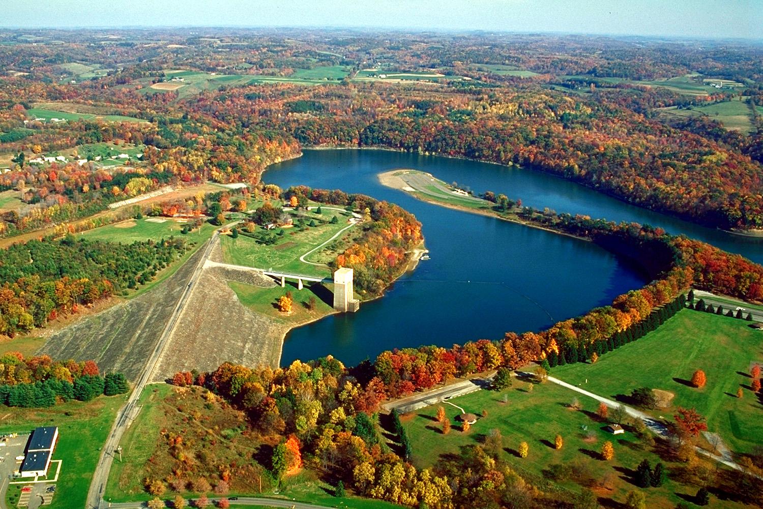 Aerial view of a winding lake and dam surrounded by vibrant autumn trees.
