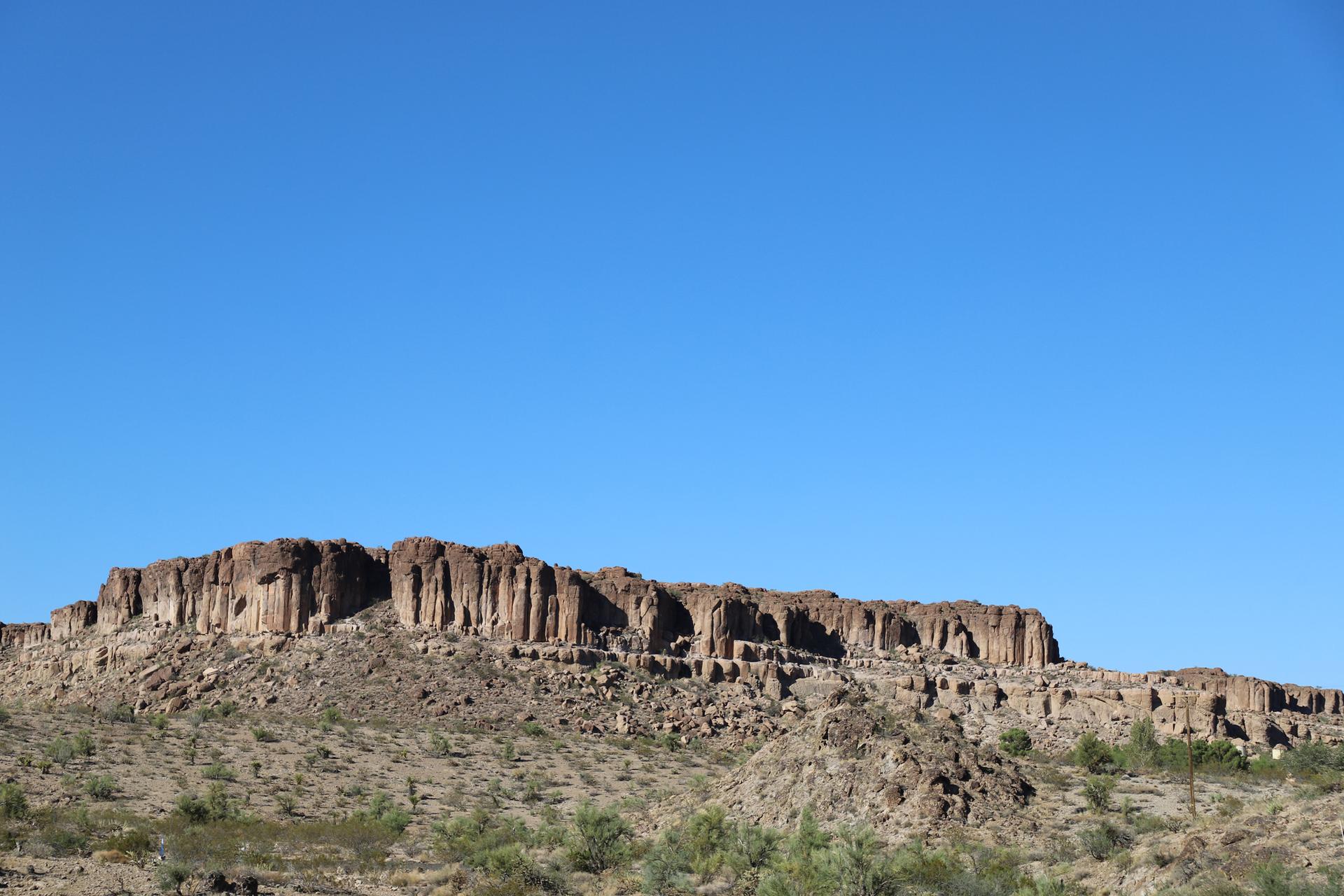 Rugged rock formation under a clear blue sky, with arid foreground.