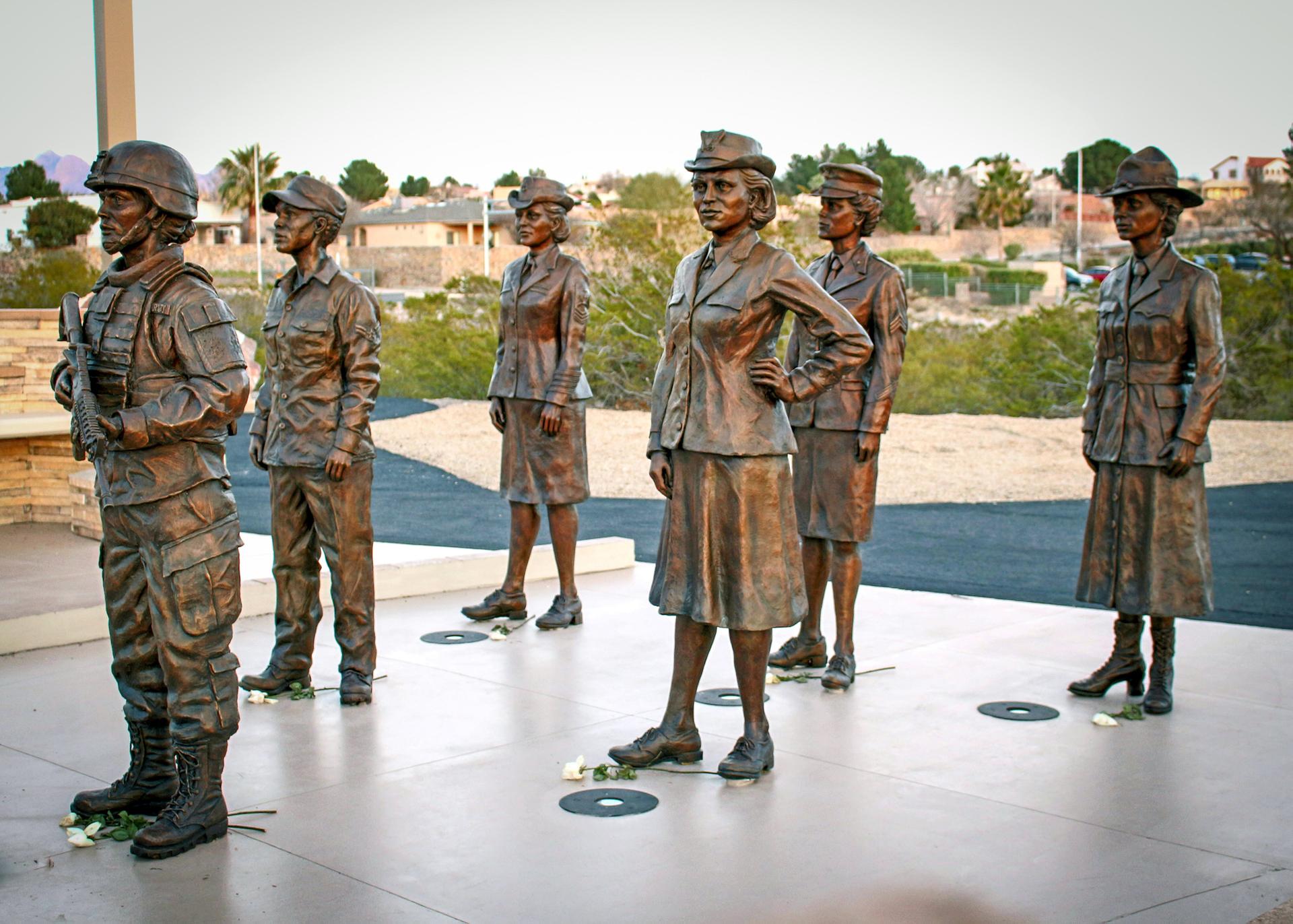 Six bronze statues of women in military uniforms stand outdoors.