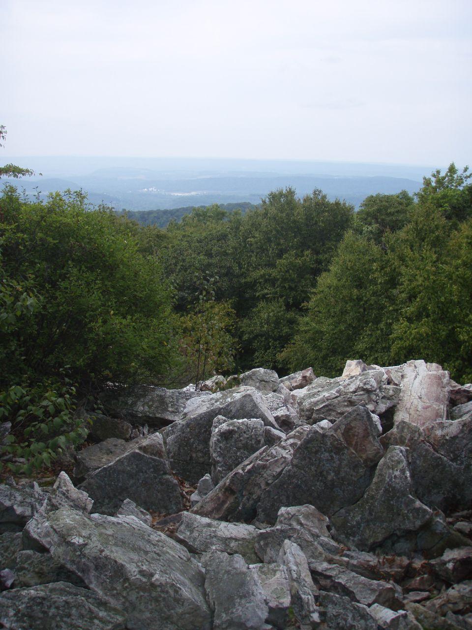 Large gray rocks in foreground, with forested hills and hazy sky.