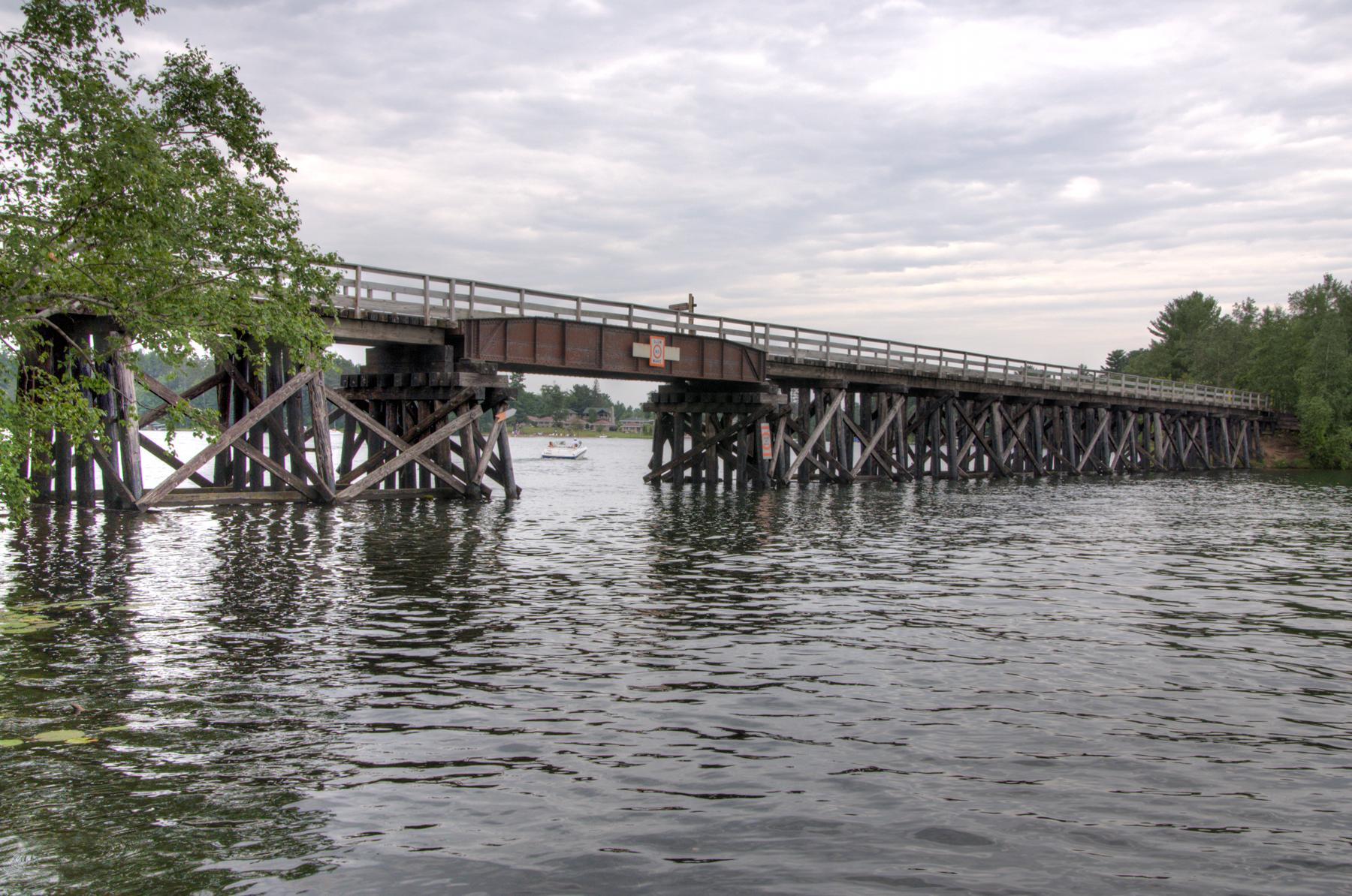 Long wooden bridge spans dark water under an overcast sky.