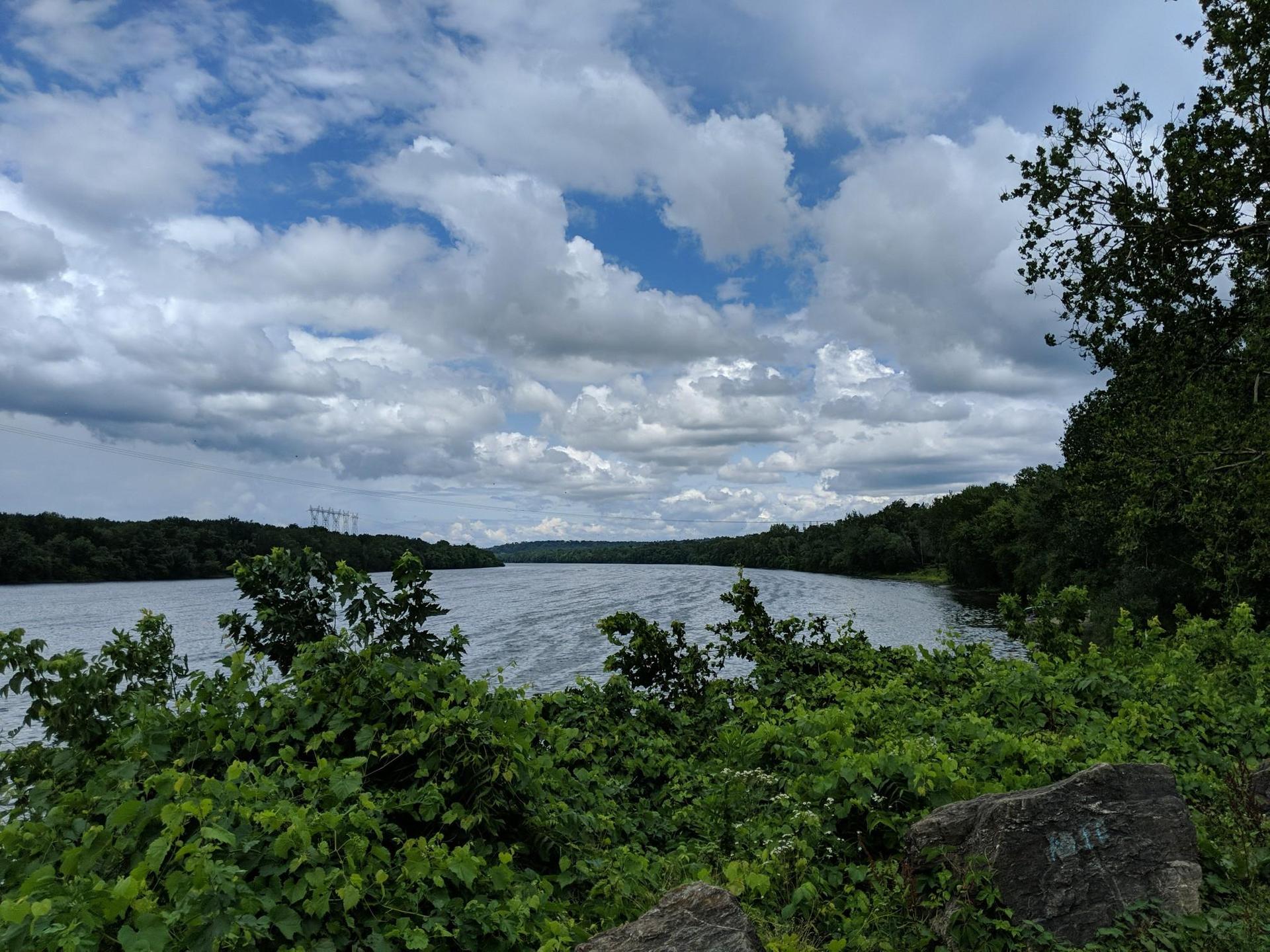 Wide river framed by dense green foliage under a dramatic cloudy sky.