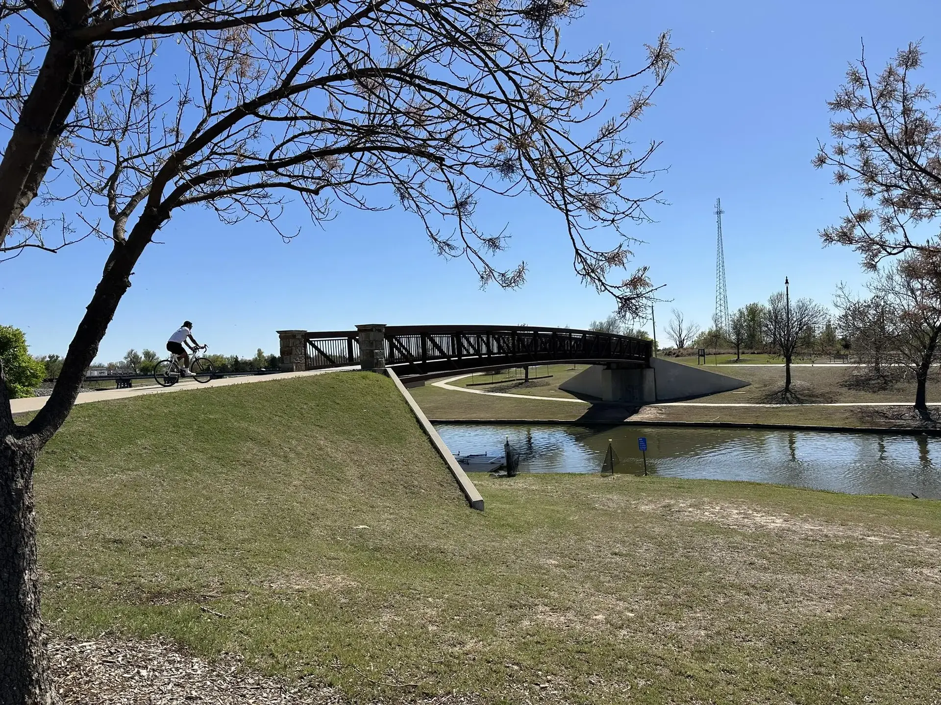 Cyclist on a paved path approaching a bridge over water, bright day.