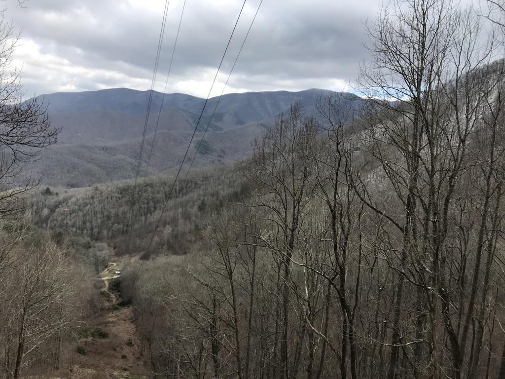 Overcast view of a vast mountain range and valley with bare trees.