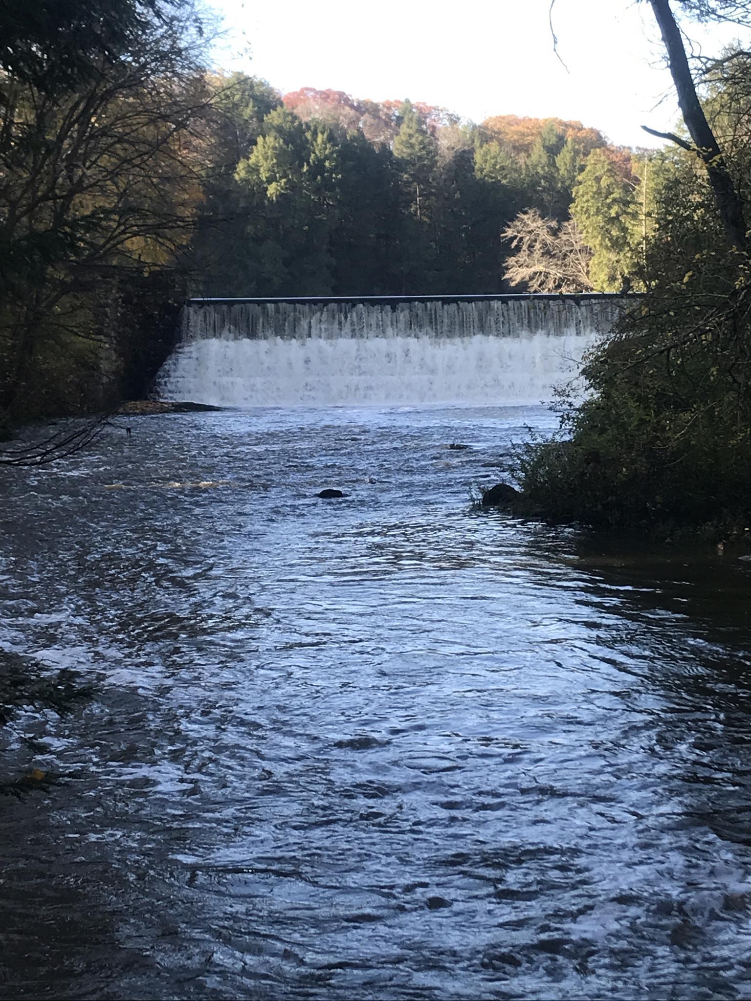 A wide waterfall over a dam, with a river flowing under a cloudy sky.