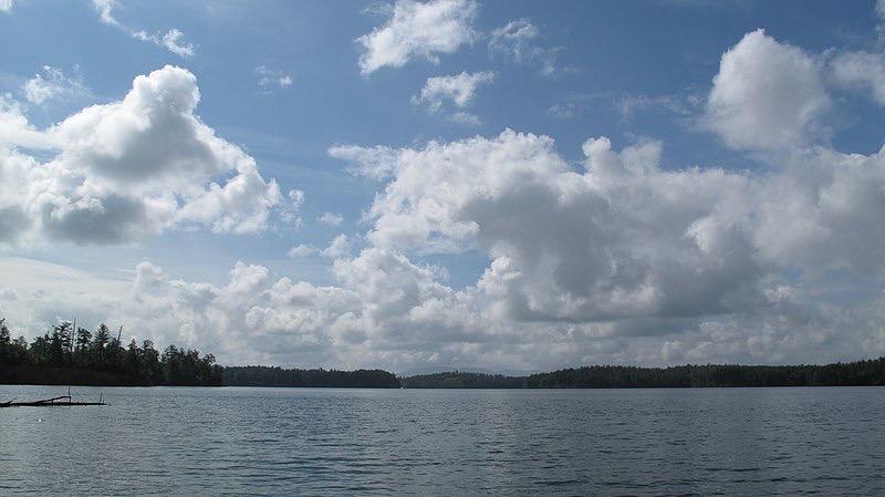 A wide lake with forested shores under a bright, partly cloudy sky.