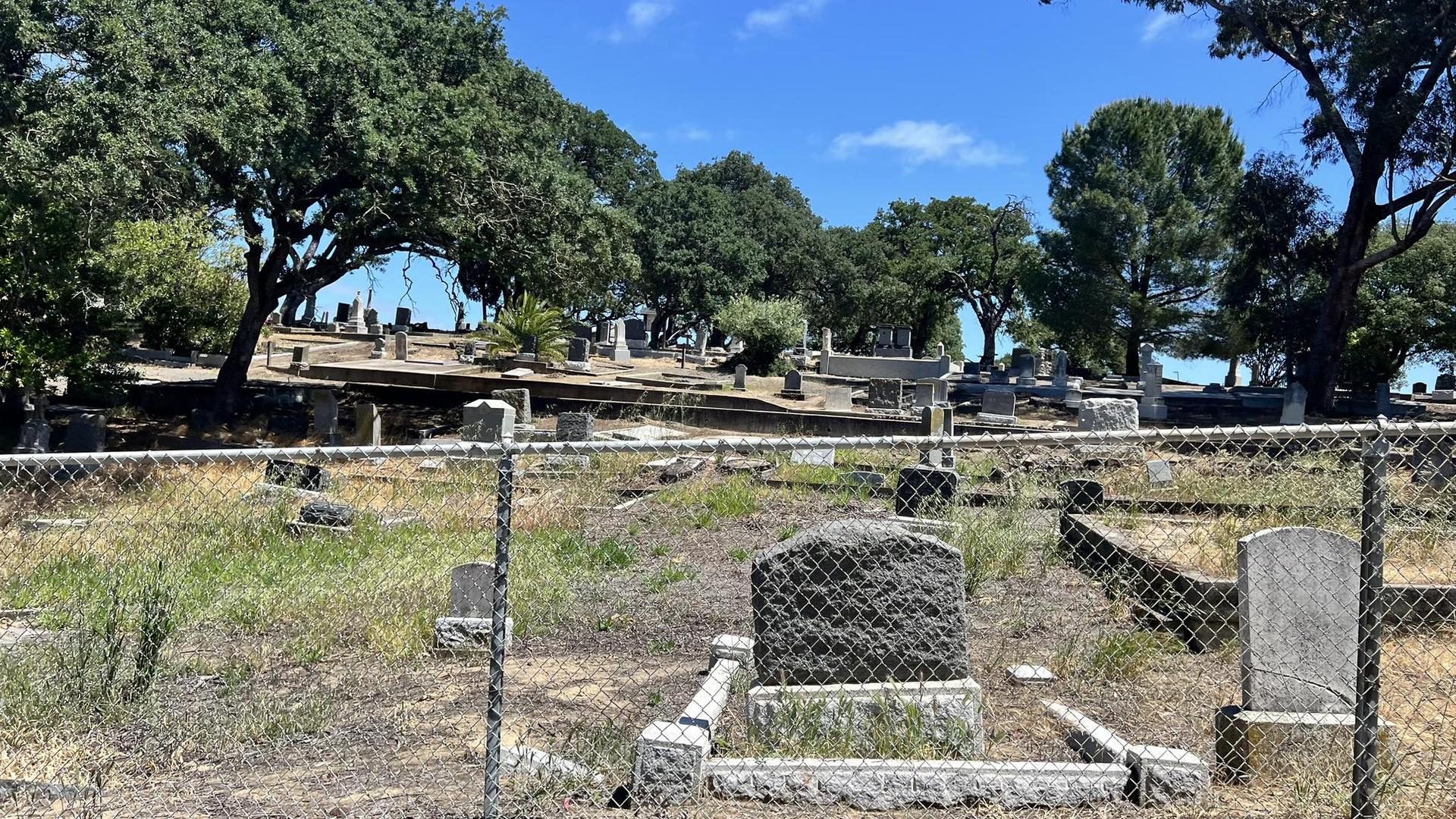 Sunny view of an old cemetery with gravestones behind a fence.