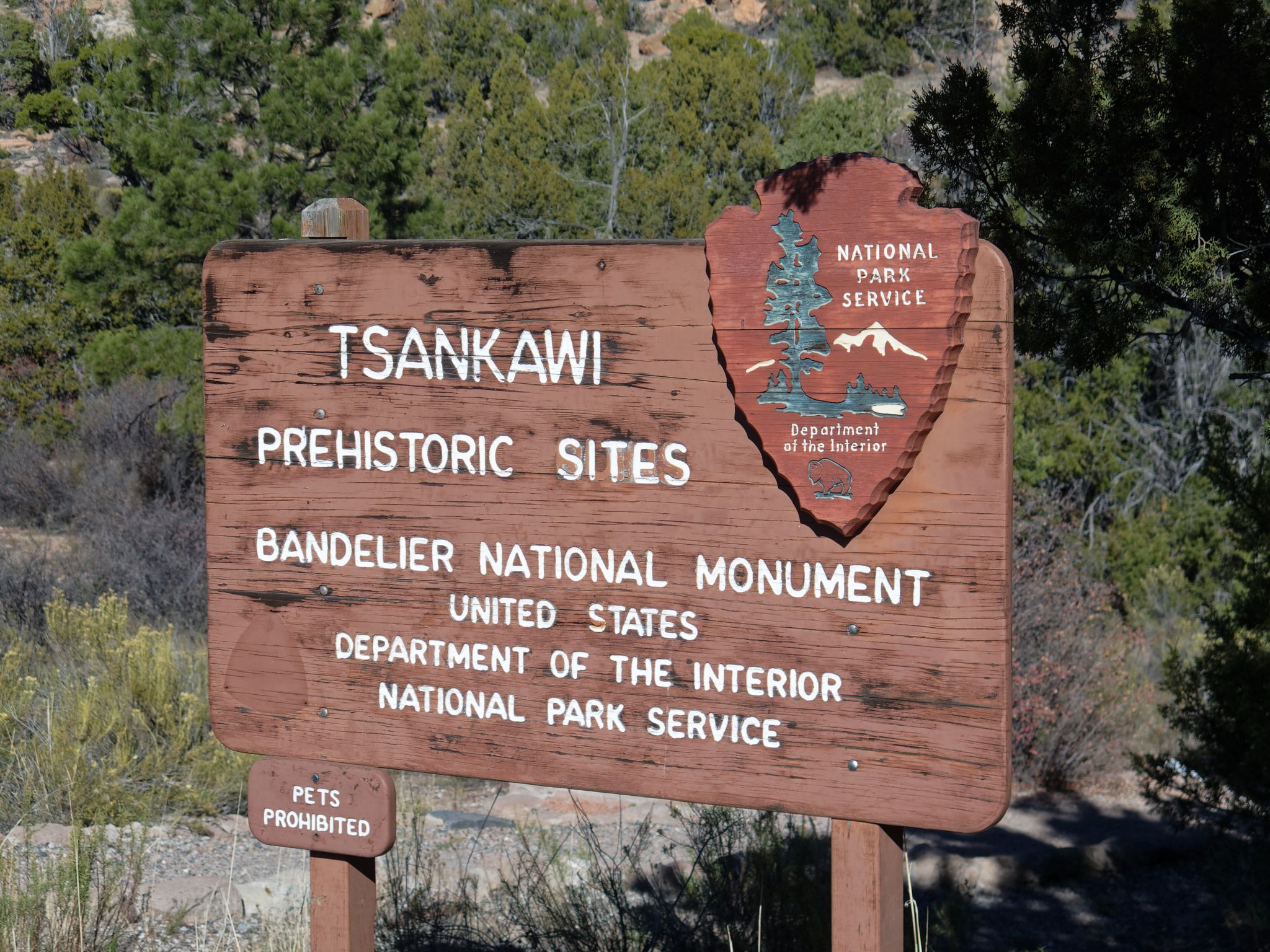 Wooden sign for a prehistoric site, with a national park service emblem. - Tsankawi Section Trailhead loop from Tsankawi Pueblo