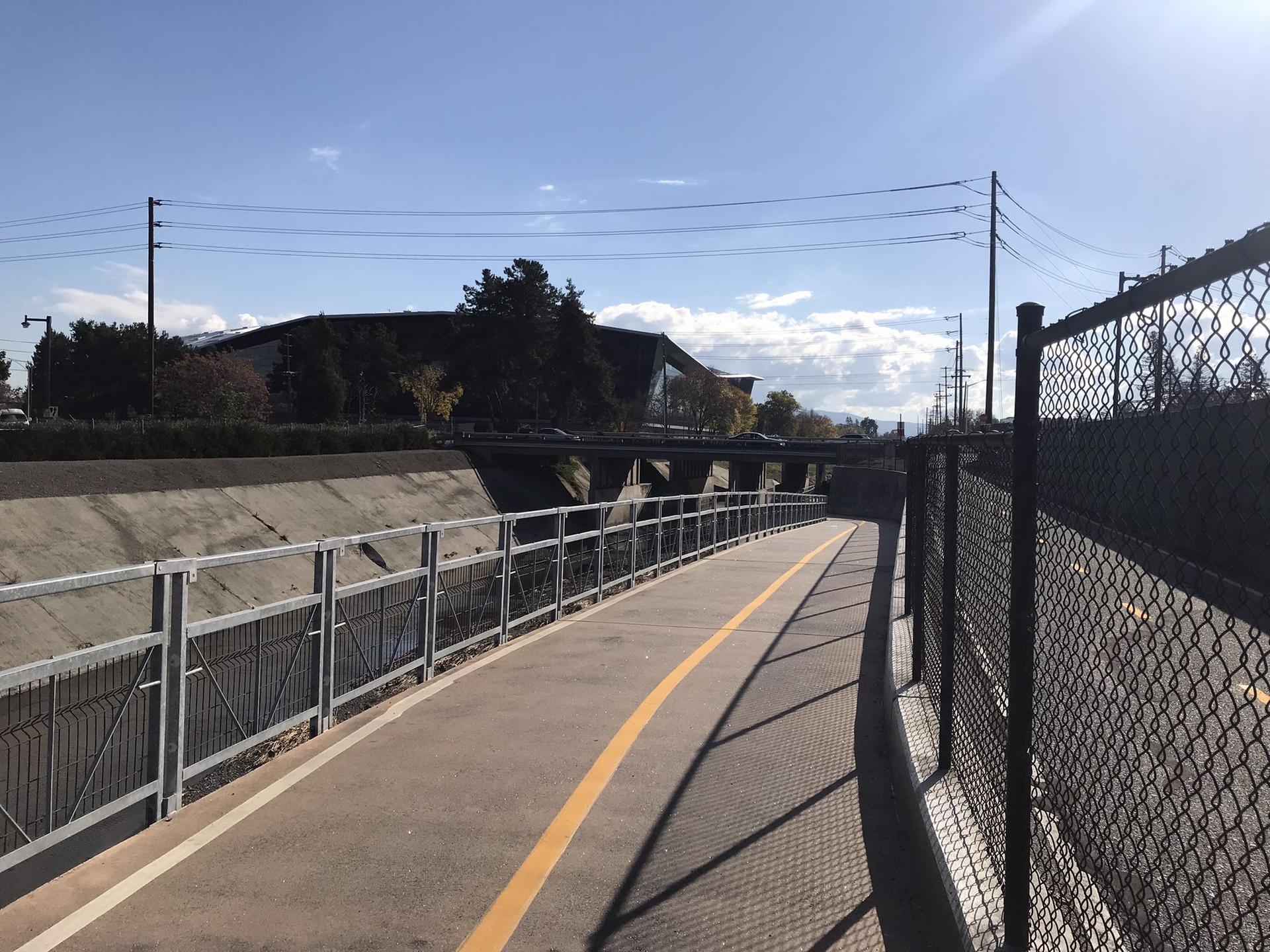 Paved path with yellow line next to a concrete canal on a sunny day.