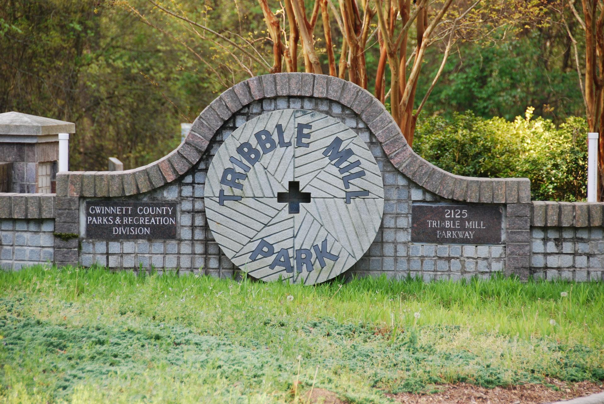 Stone and brick park sign with a large wooden mill wheel design.