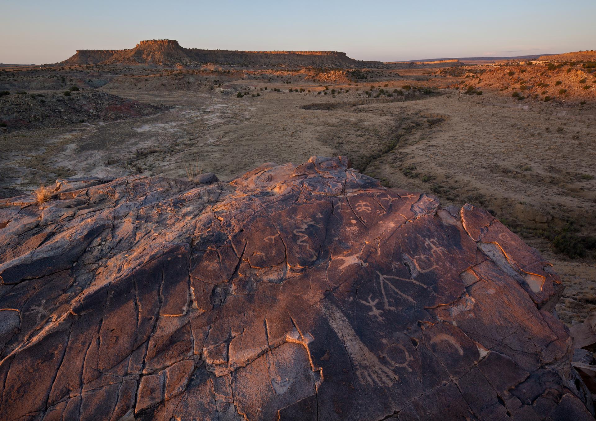 Wide desert landscape at sunset, with ancient petroglyphs on foreground rock.