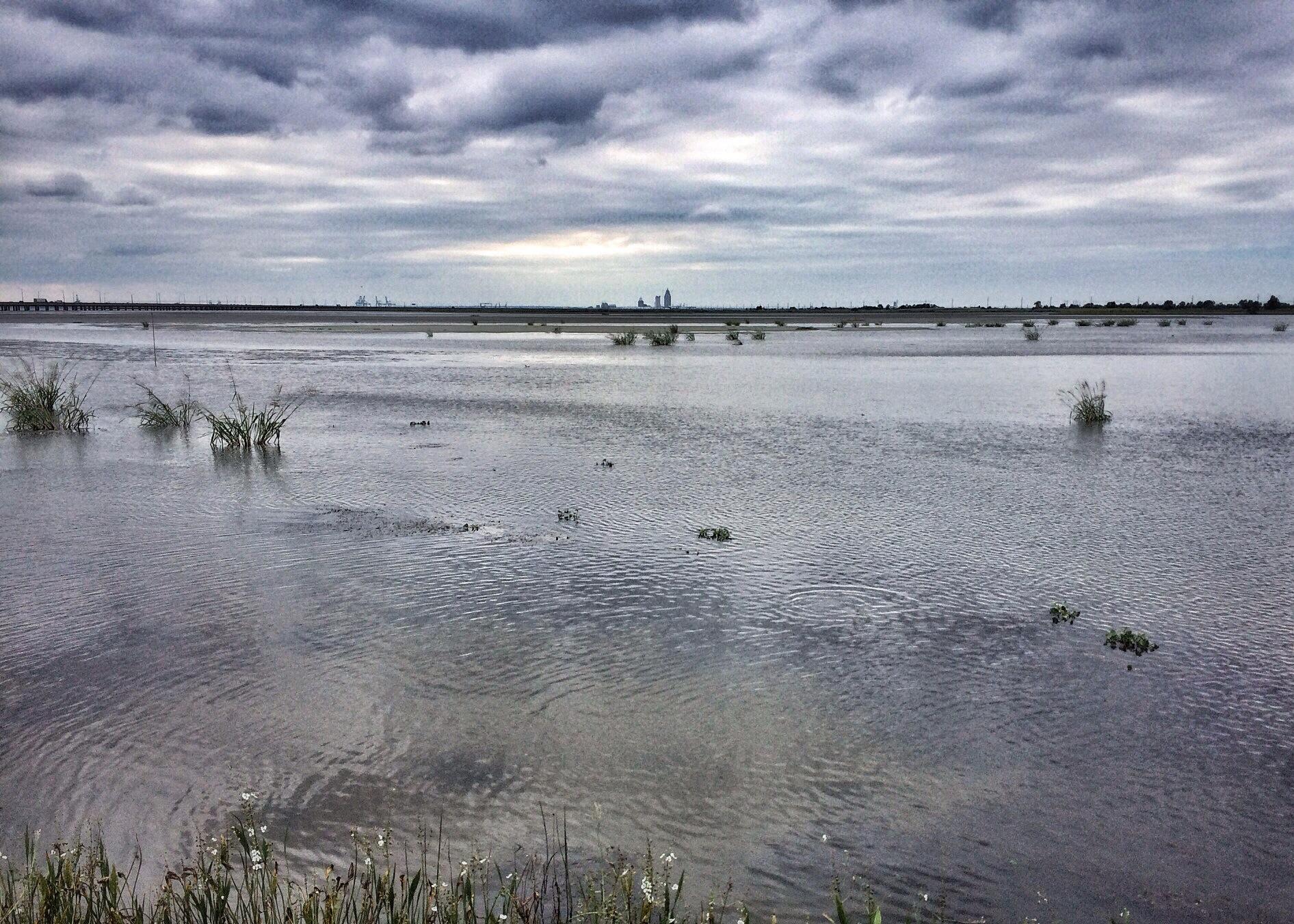 A wide, calm body of water under a dramatic cloudy sky.