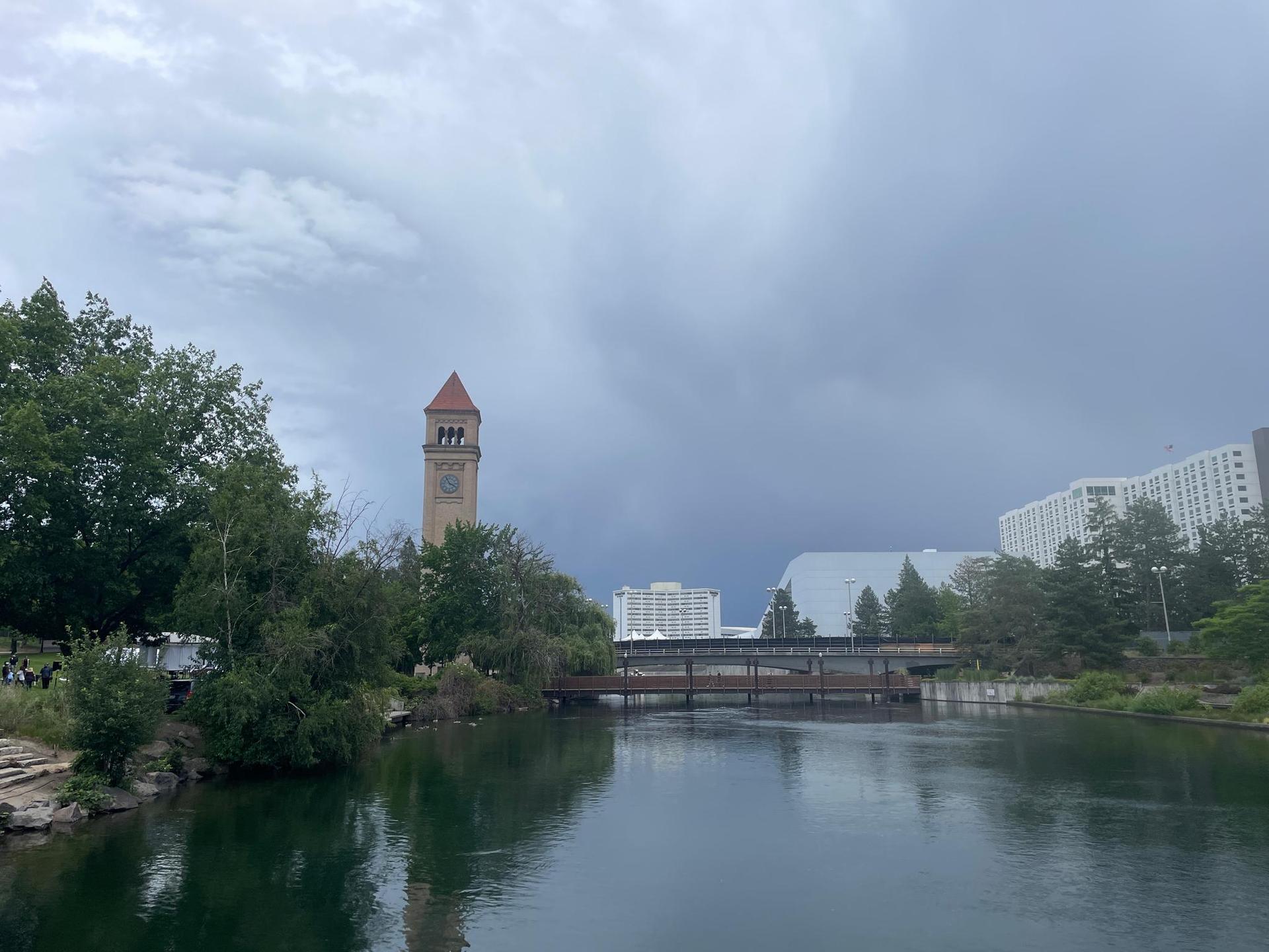 Calm river reflecting a cloudy sky, with a clock tower and modern buildings.