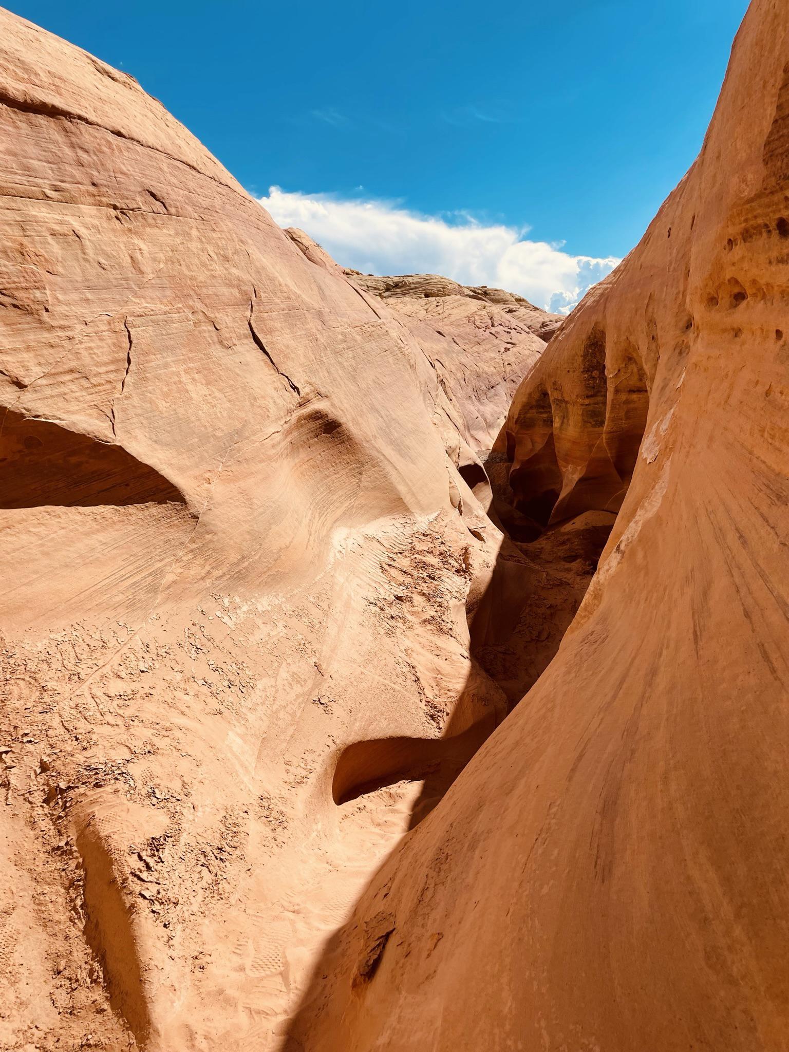 Winding slot canyon with smooth, curved orange rock walls, bright light.