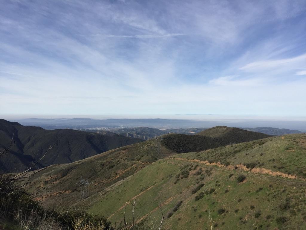 Expansive view of rolling green and brown hills under a cloudy sky.