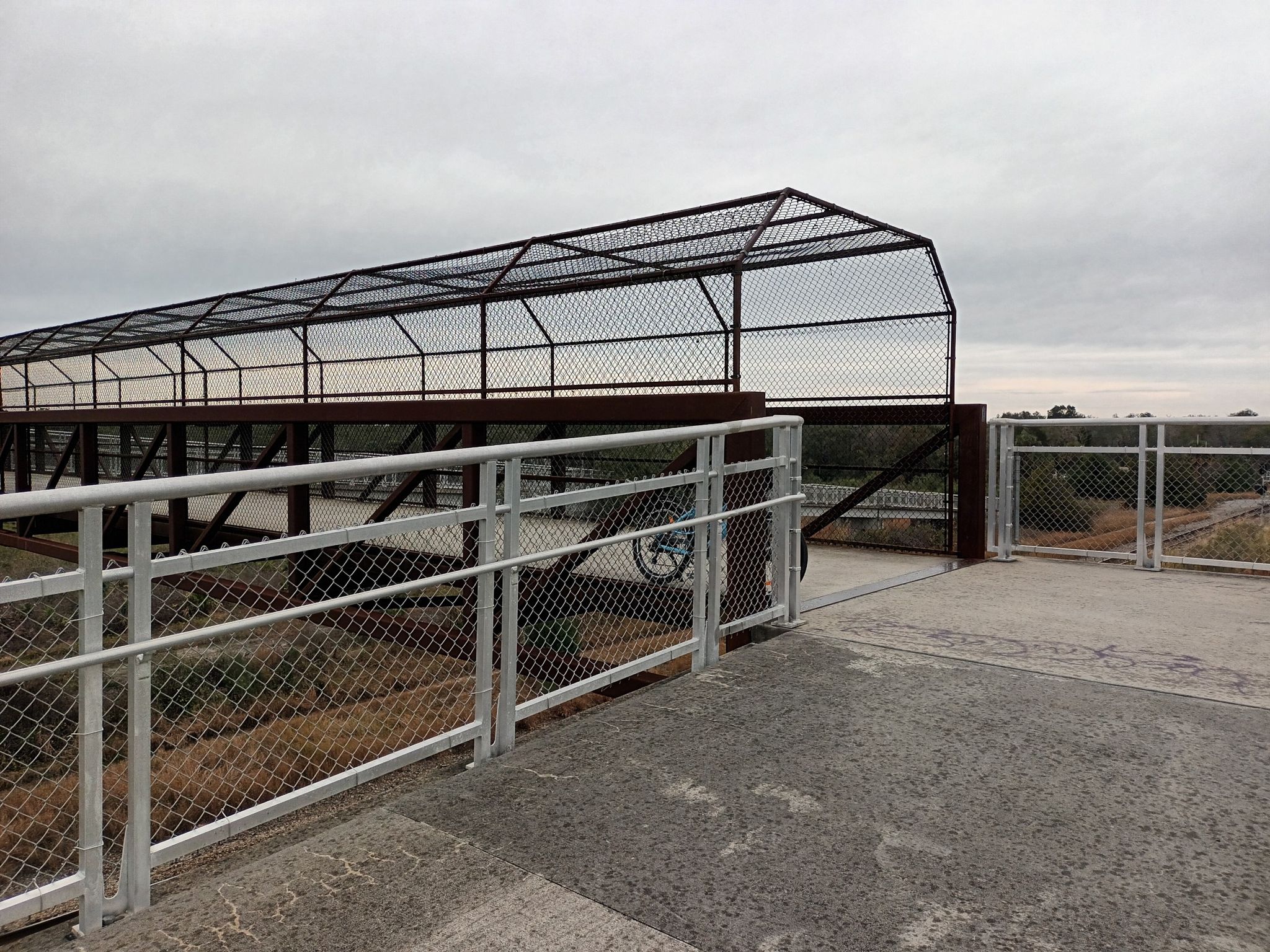 A covered pedestrian bridge with chain link fencing under an overcast sky. - New Smyrna Beach to Lake Beresford via East Coast Greenway loop