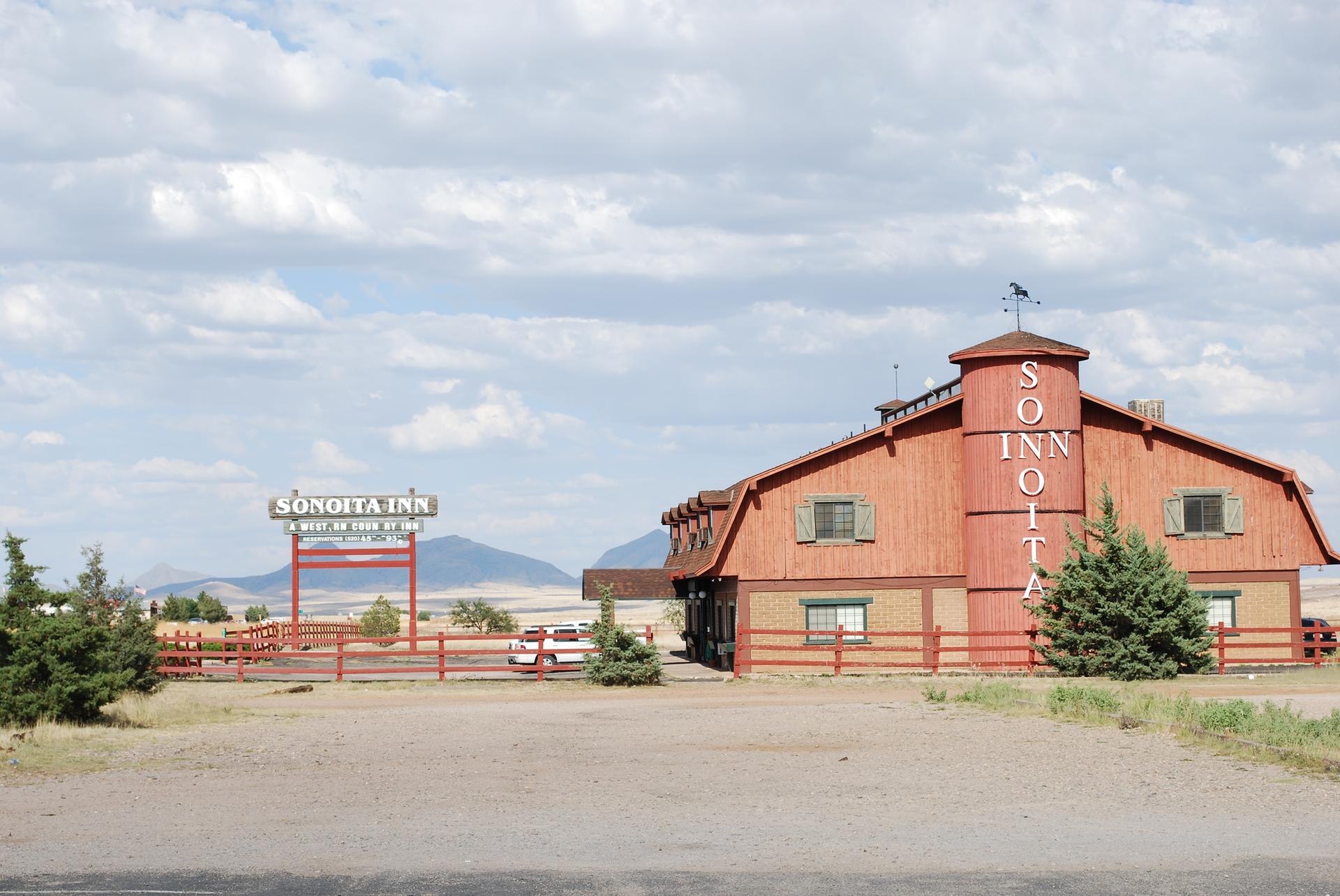 A red barn-style building with a sign, surrounded by dry landscape under cloudy skies.