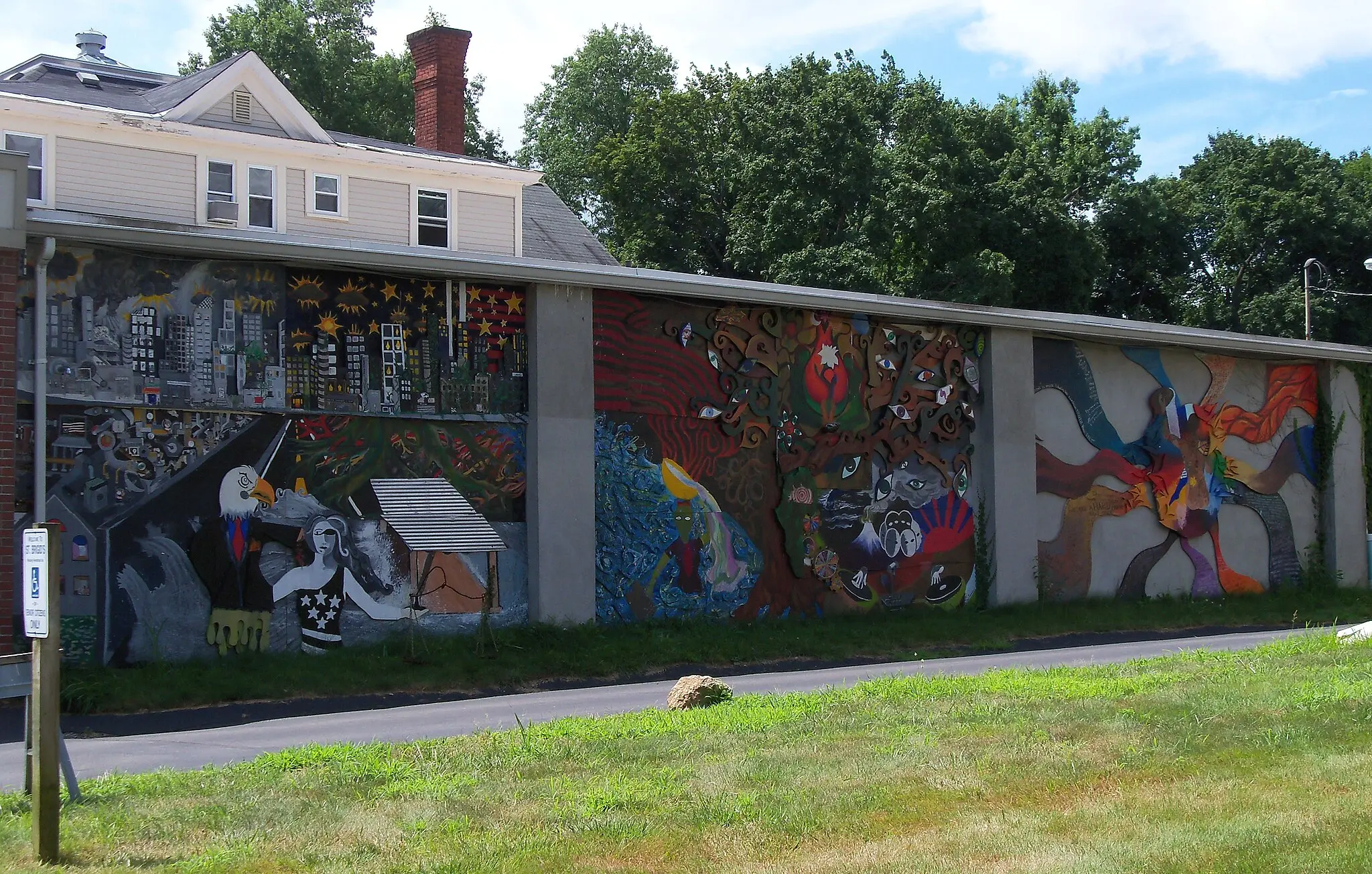 A vibrant, colorful mural covers a long building wall under bright daylight.