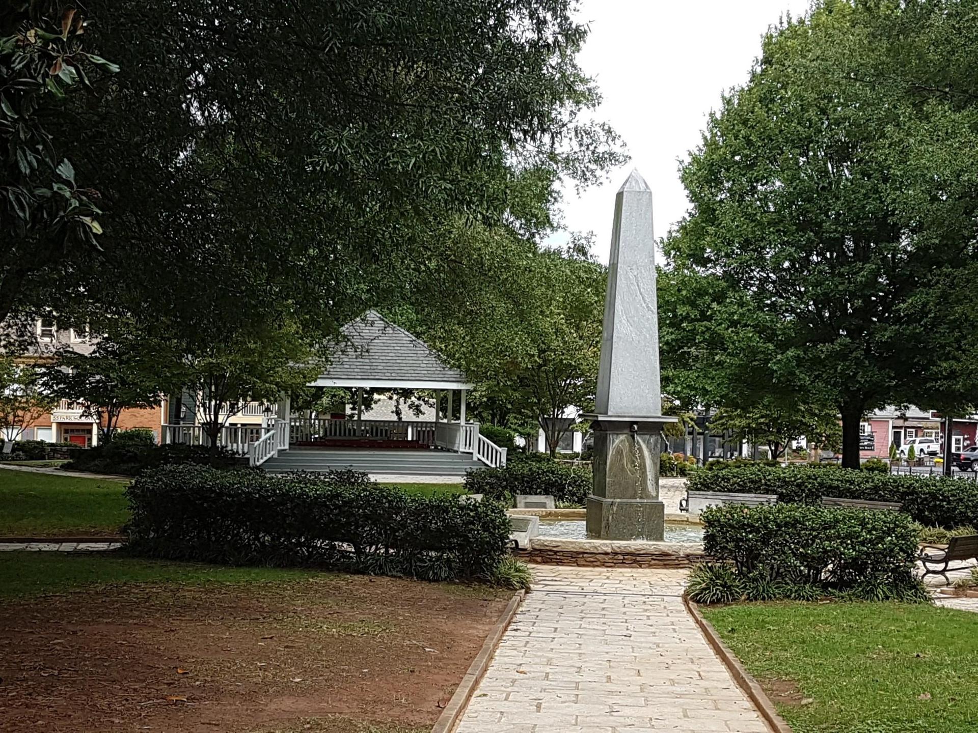A park scene with a tall obelisk, white gazebo, and green trees.