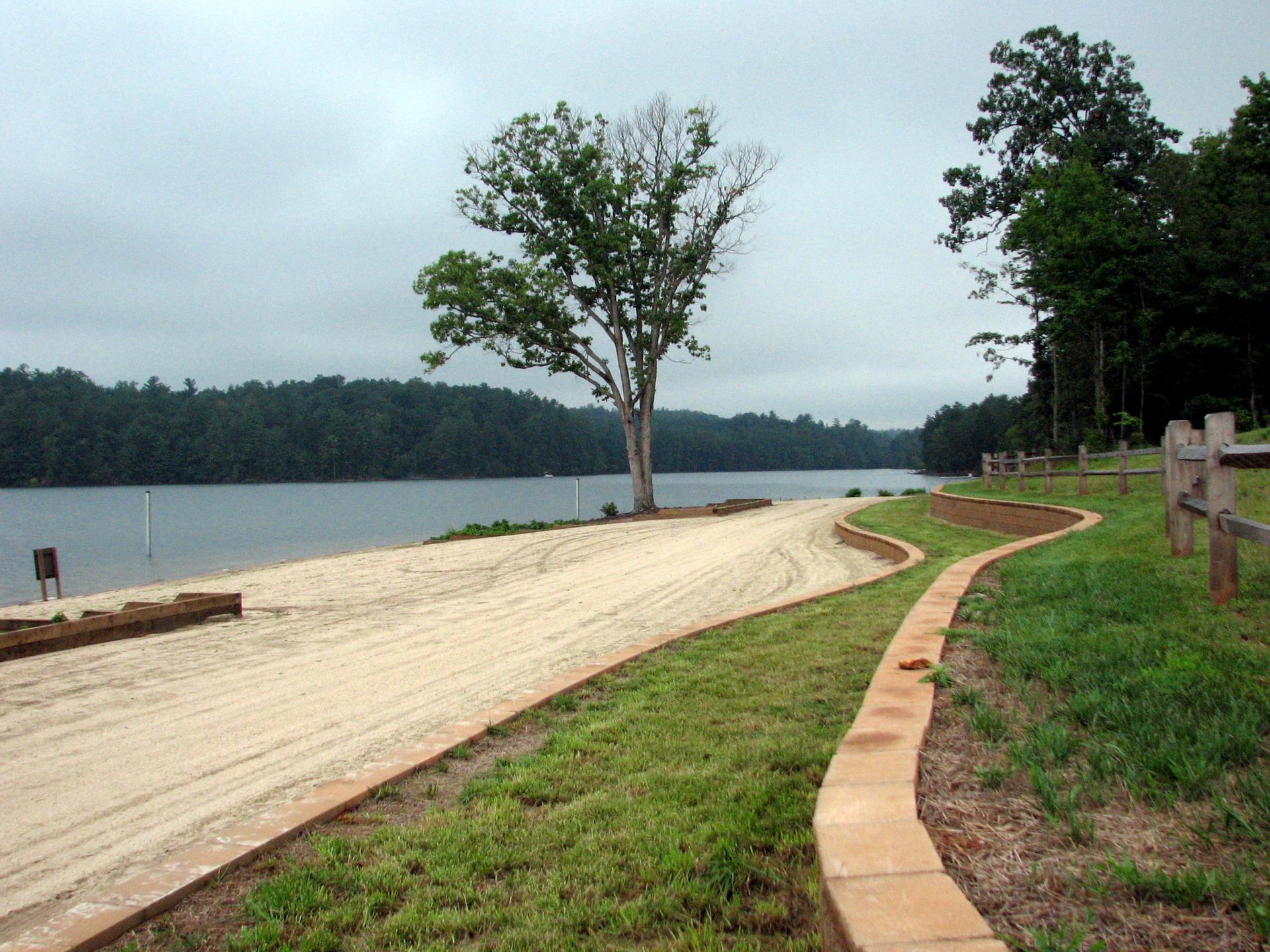 Sandy path curves towards a calm lake under an overcast sky.