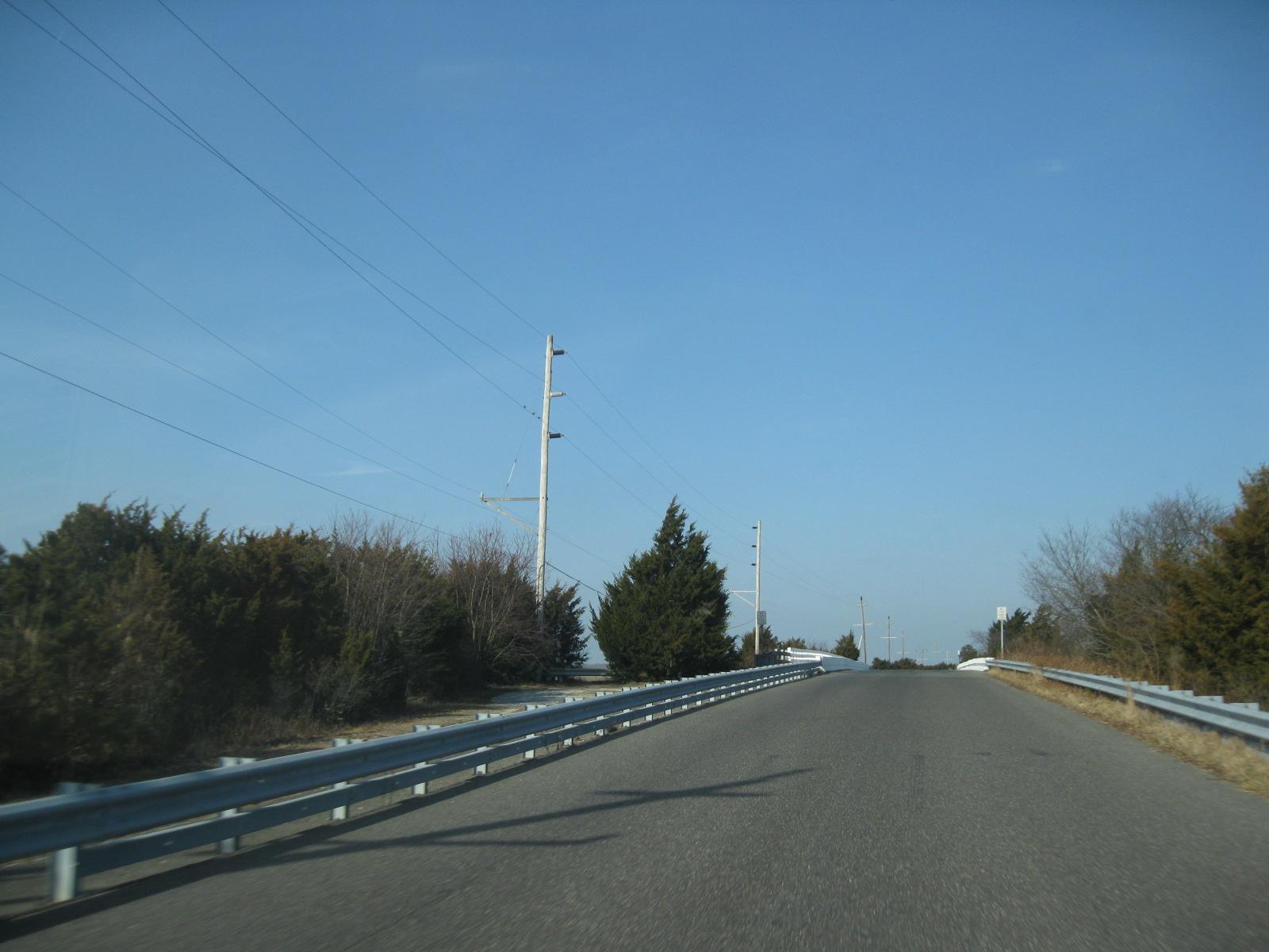 Empty paved road with guardrails under clear blue sky.