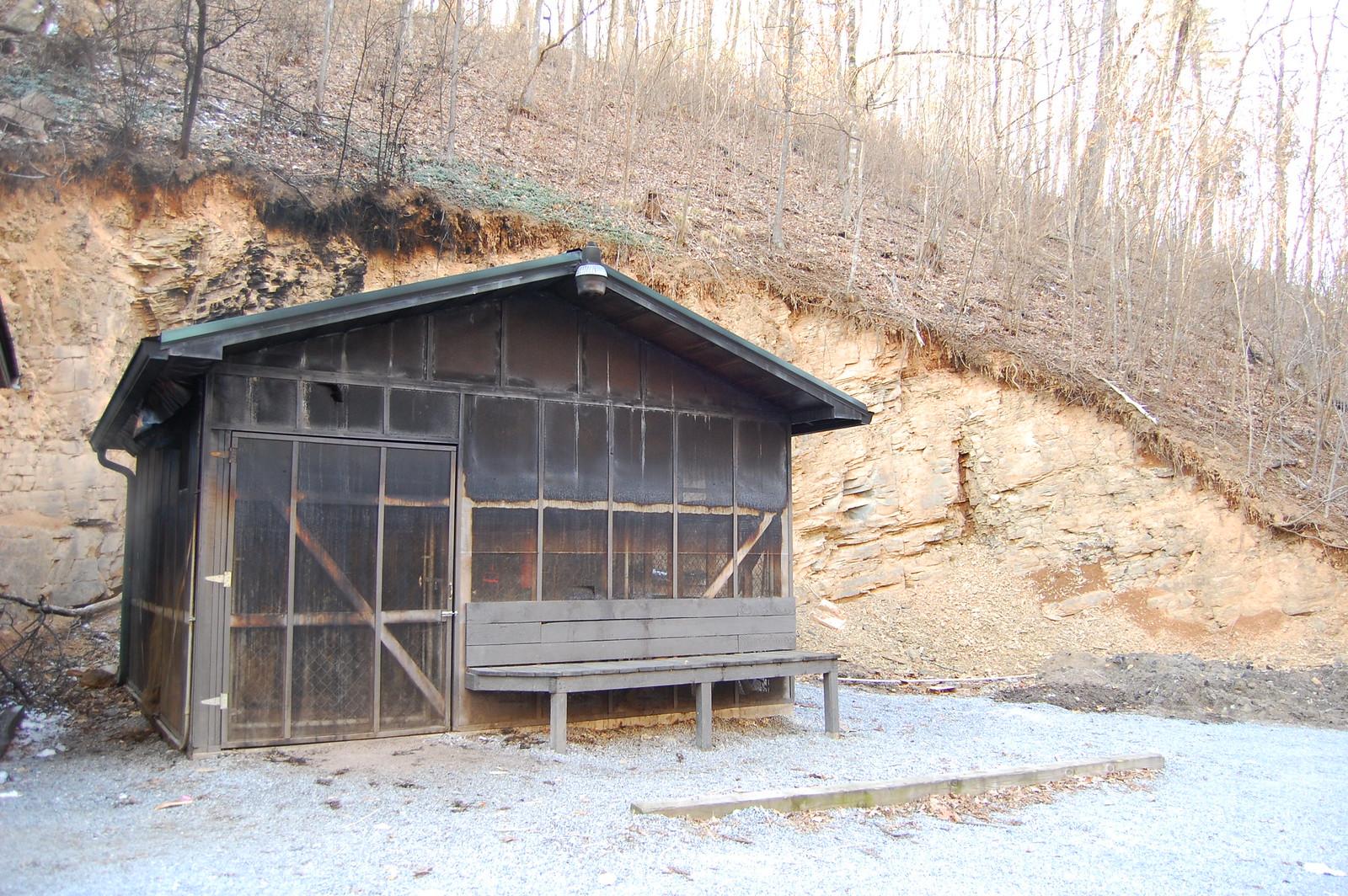 Small wooden cabin with a bench next to a dirt hillside.