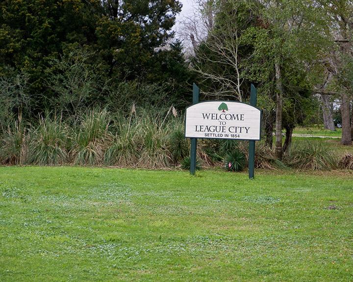 Wooden sign in a grassy field with dense green trees behind it.