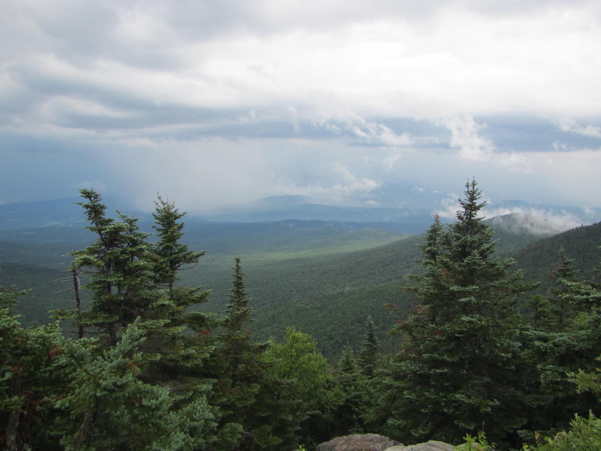 Panoramic view of vast forested mountains under a dramatic, cloudy sky.