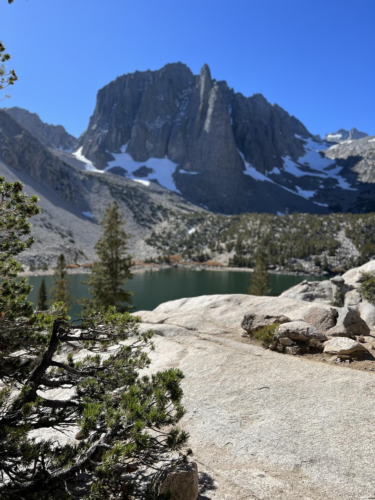 Distant snow-capped jagged mountain peak overlooking a dark lake, sunny day.