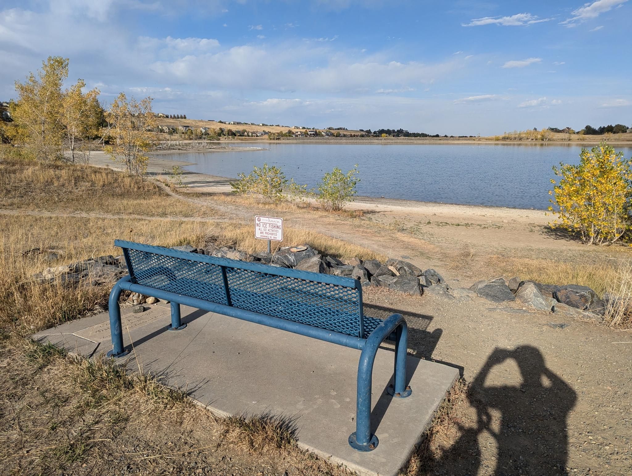 A blue metal bench overlooks a lake with dry shores under a sunny sky. - Tucker Lake Trail