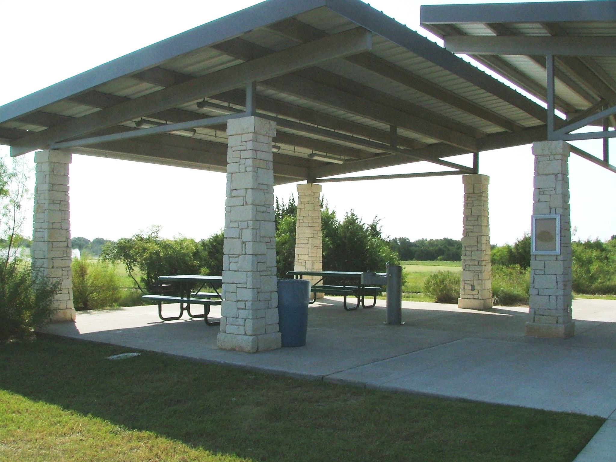 An empty outdoor pavilion with picnic tables and benches under bright daylight.