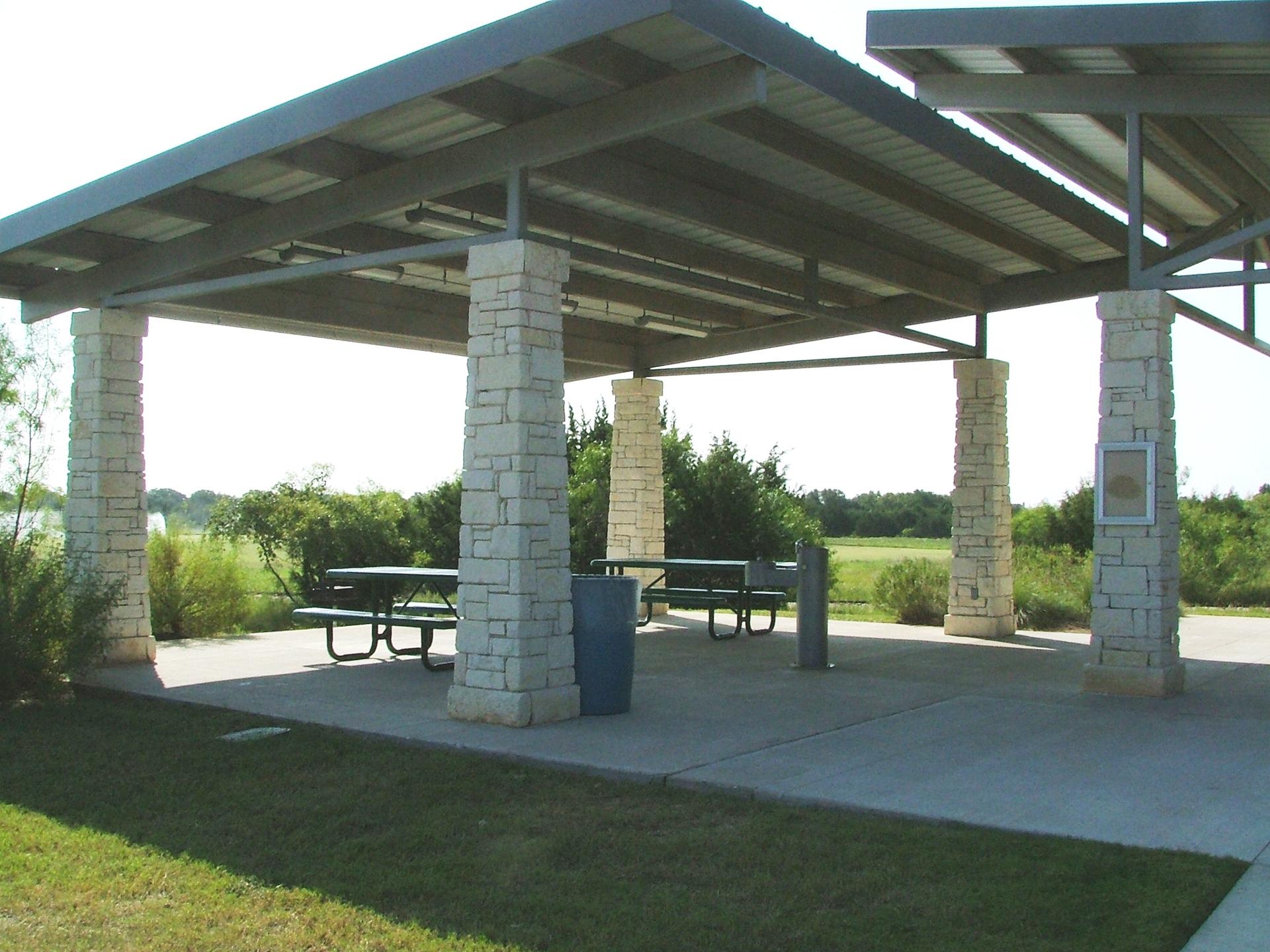 An empty outdoor pavilion with picnic tables and benches under bright daylight.