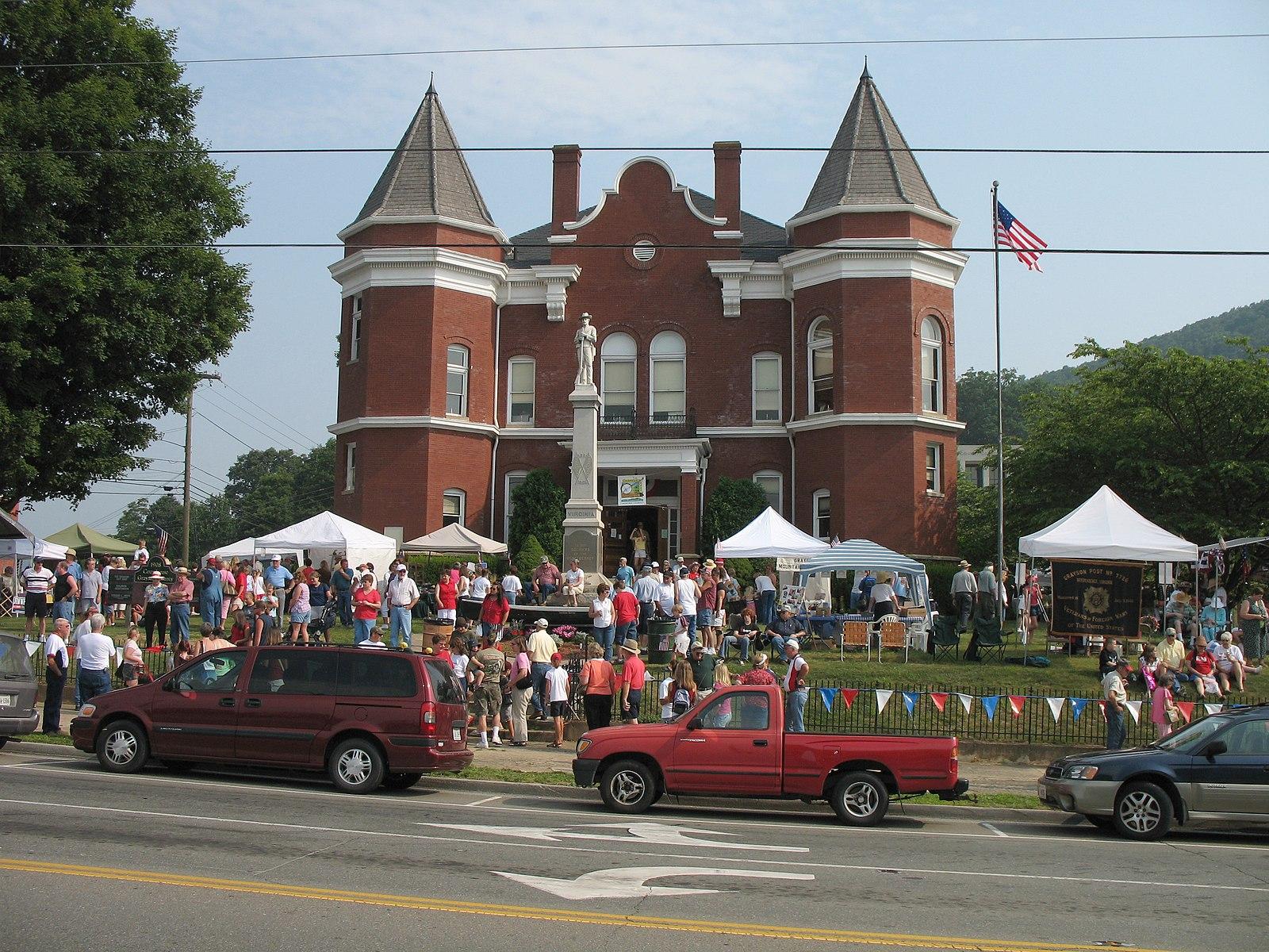 Red brick building with turrets, people gathered at an outdoor event on a sunny day.